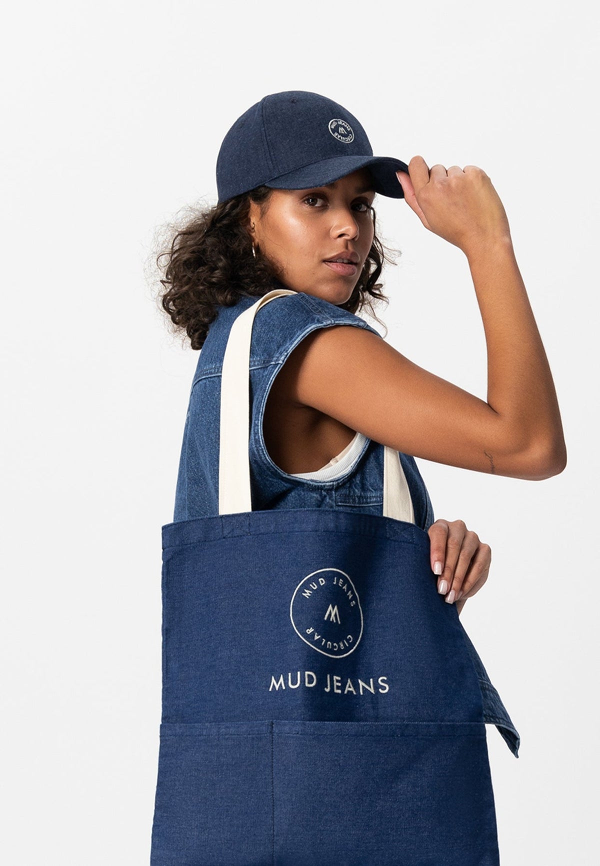 Sustainable MUD Jeans denim apron paired with a cream hoodie and ivory beanie, showcasing ethical fashion choices.