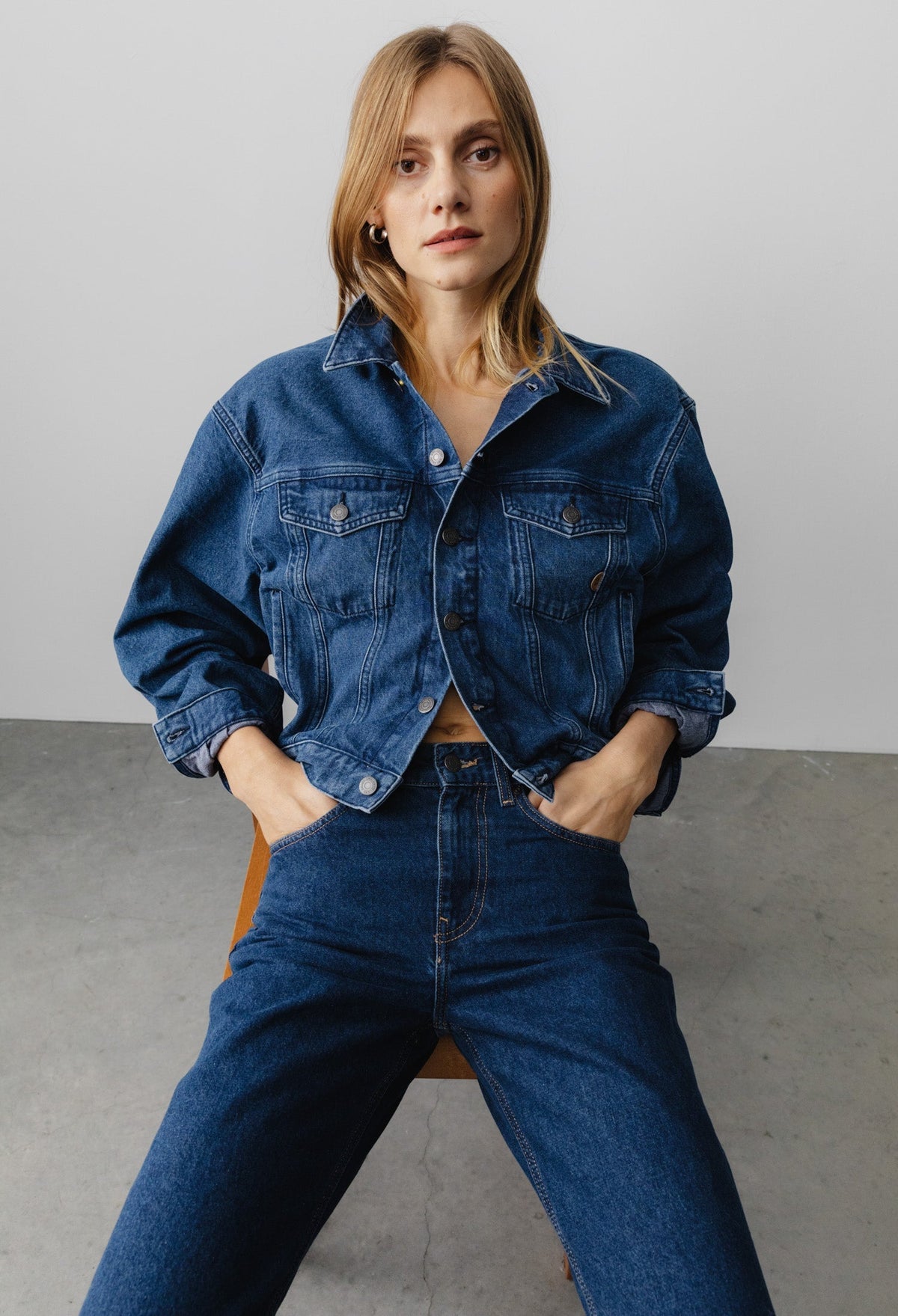 Woman wearing a classic denim jacket with matching high-waisted jeans, styled in a casual fashion on a minimalist background.