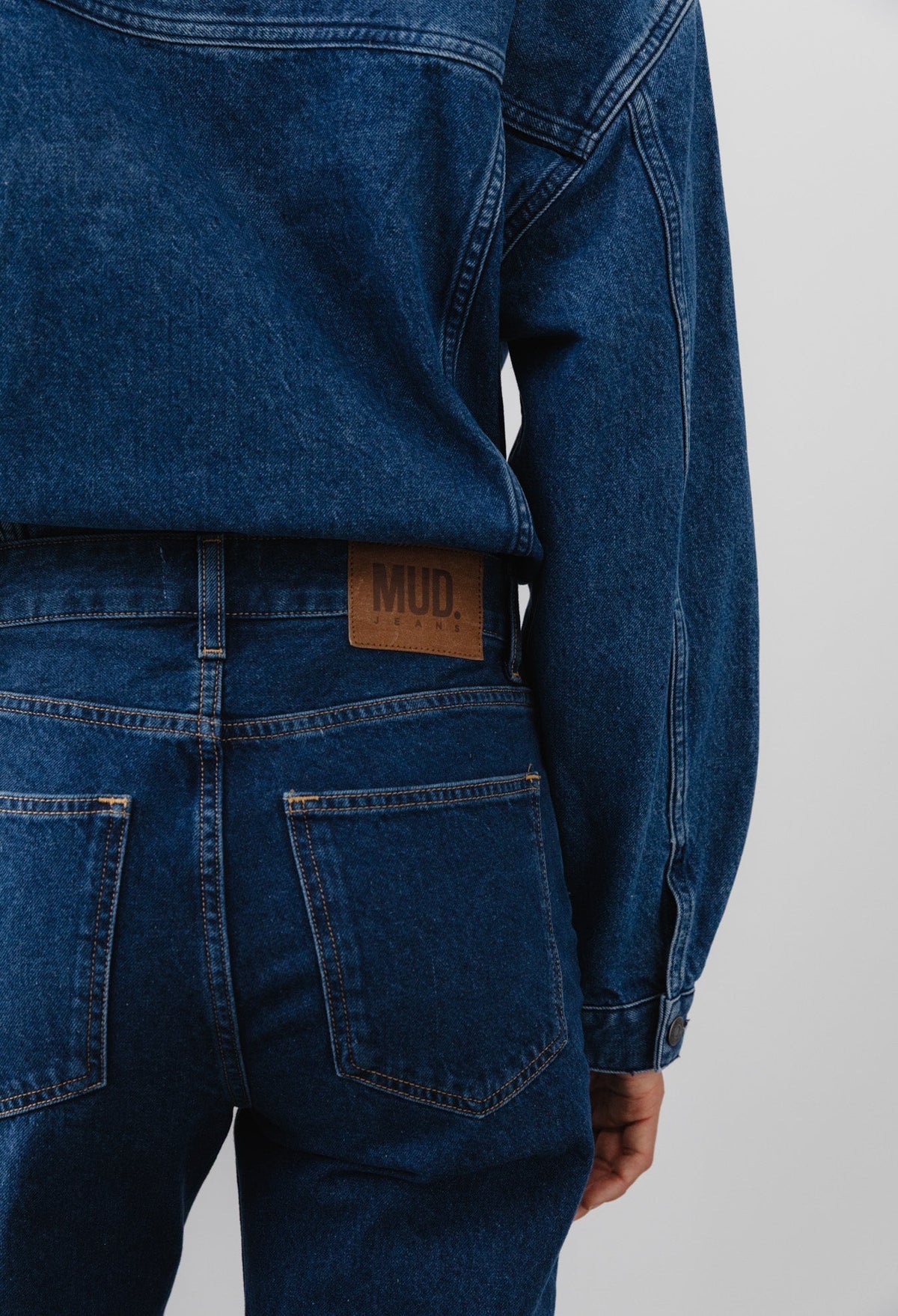 Back view of recycled dark blue denim jacket and jeans set, featuring MUD Jeans logo on leather patch above pocket.