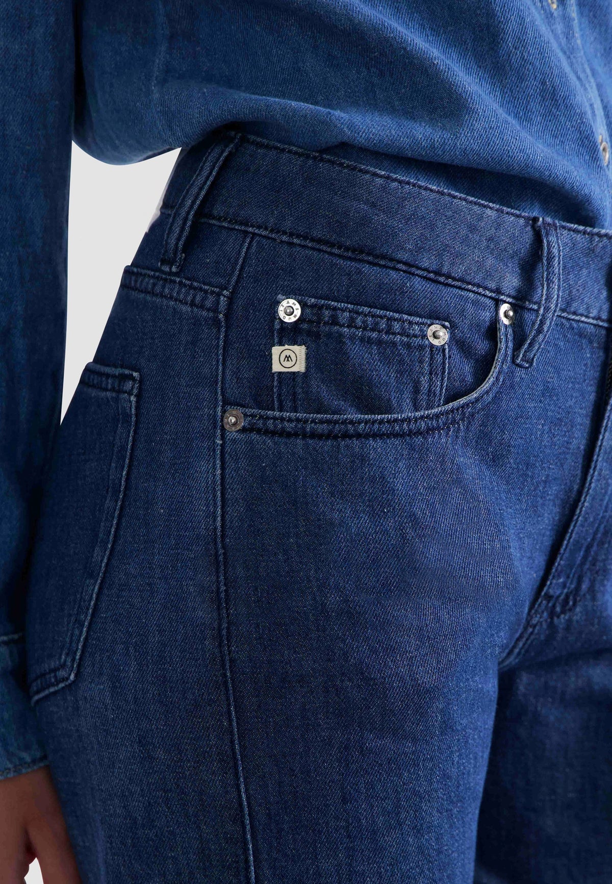 Dark blue denim jeans with silver button accents, featuring a close-up on the pocket and stitching details.
