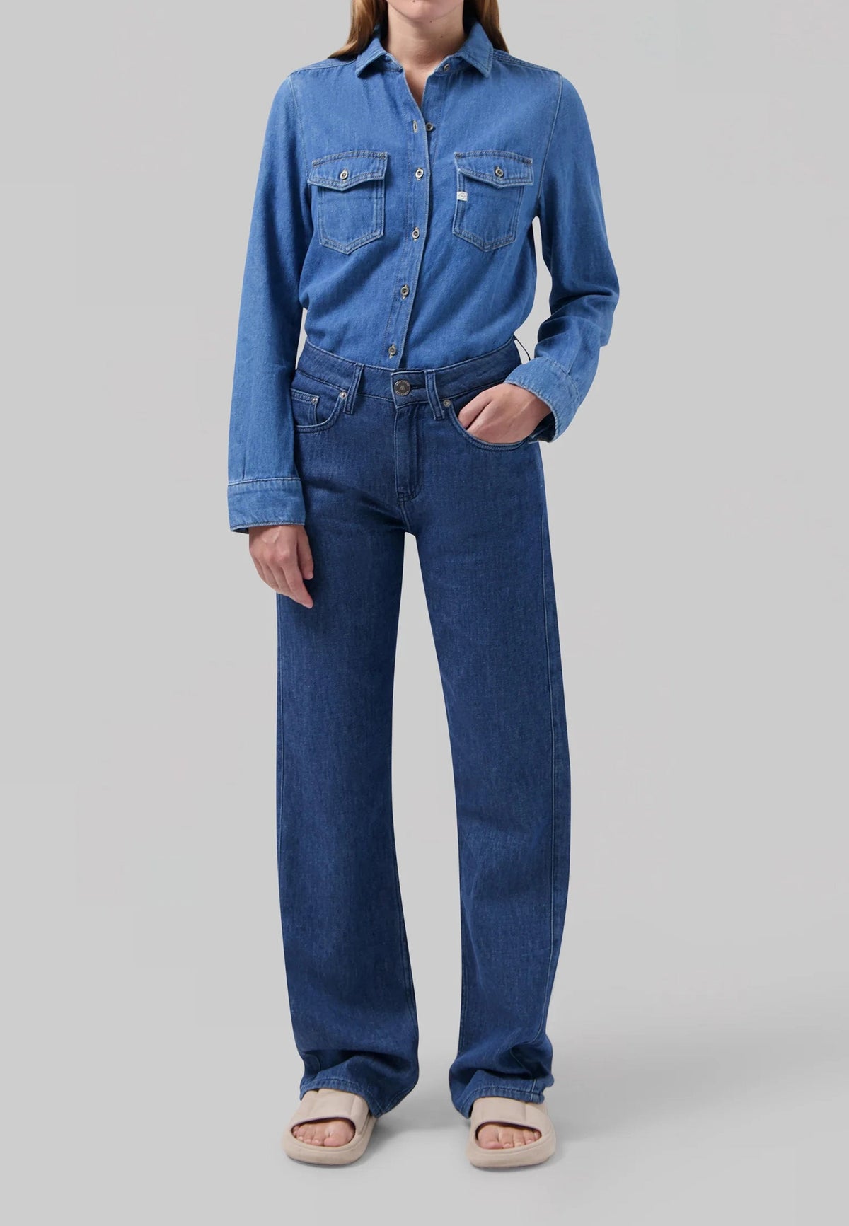 Casual outfit featuring a denim shirt with buttoned front pockets and matching straight-leg jeans, paired with cream sandals.