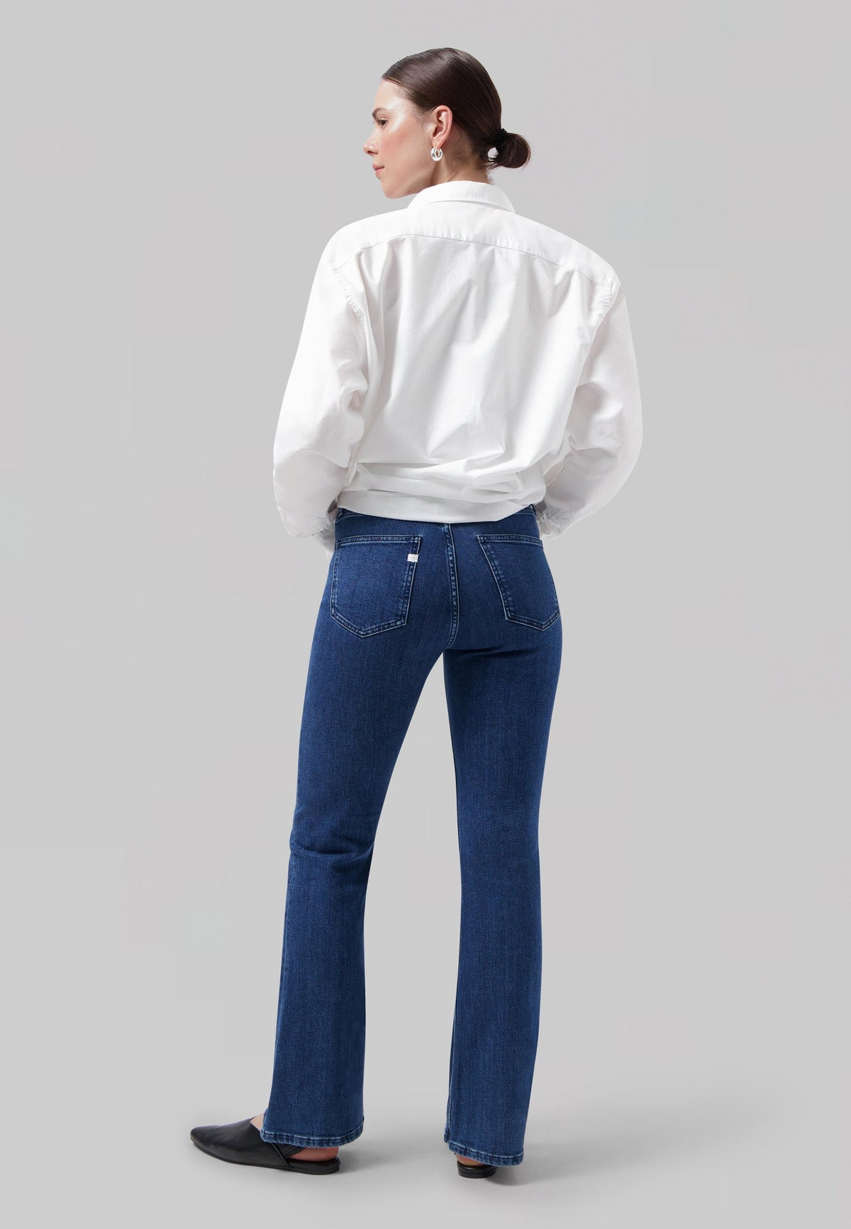 A model in a crisp white shirt and tailored blue jeans, showcasing a classic minimalist fashion look against a gray background.