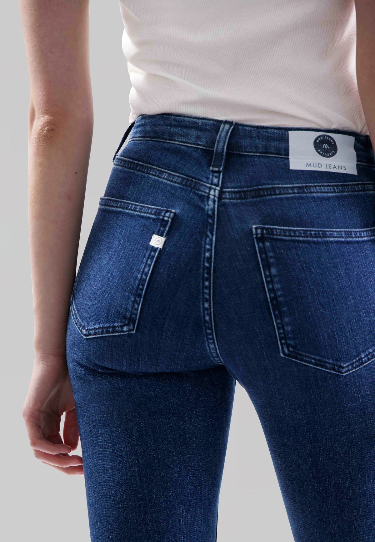 Back view of MUD Jeans made from organic cotton, showcasing blue slim-fit denim worn with a white sleeveless top.