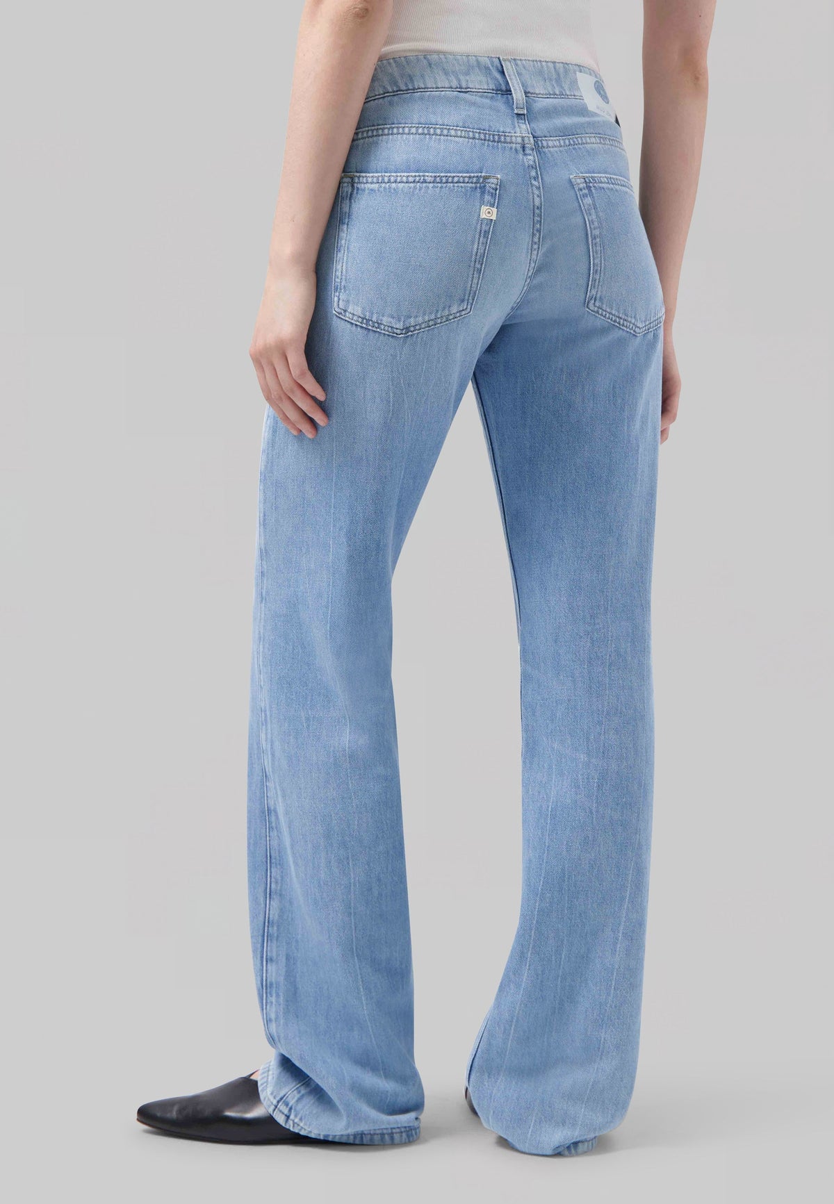 Light blue wide-leg jeans with high waist worn with a sleeveless white top, showcasing back pocket detail and black shoes.