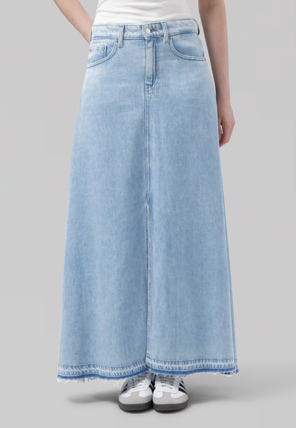 Light blue denim maxi skirt with frayed hem, worn with a white top and paired with casual white sneakers.