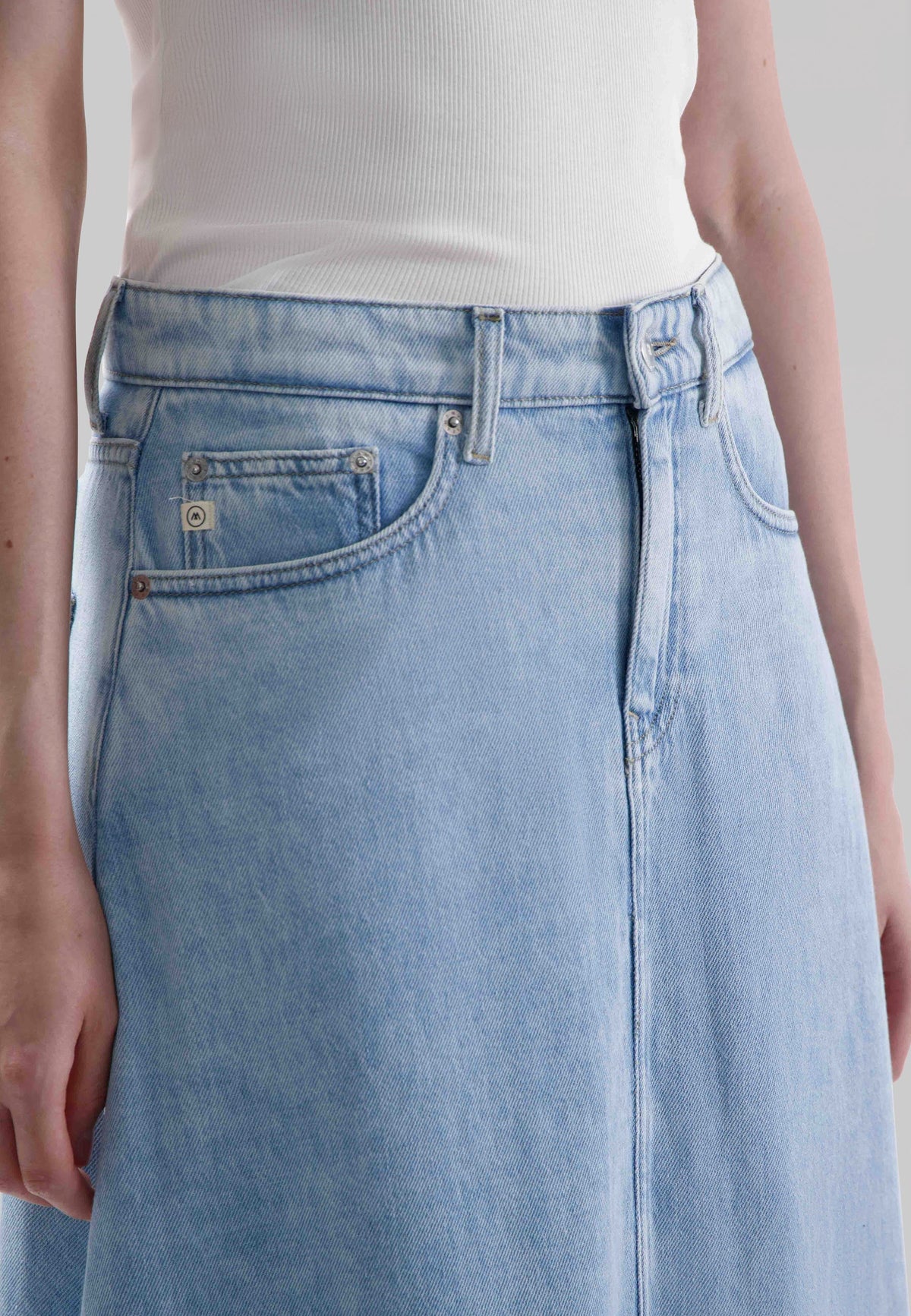 Light blue denim jeans with riveted pockets, worn with a white ribbed tank top, showcasing casual style and comfort.