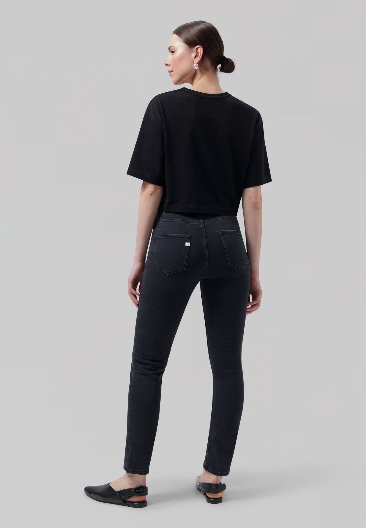 Woman wearing high-waisted black skinny jeans and a relaxed black t-shirt, styled with black slip-on flats.