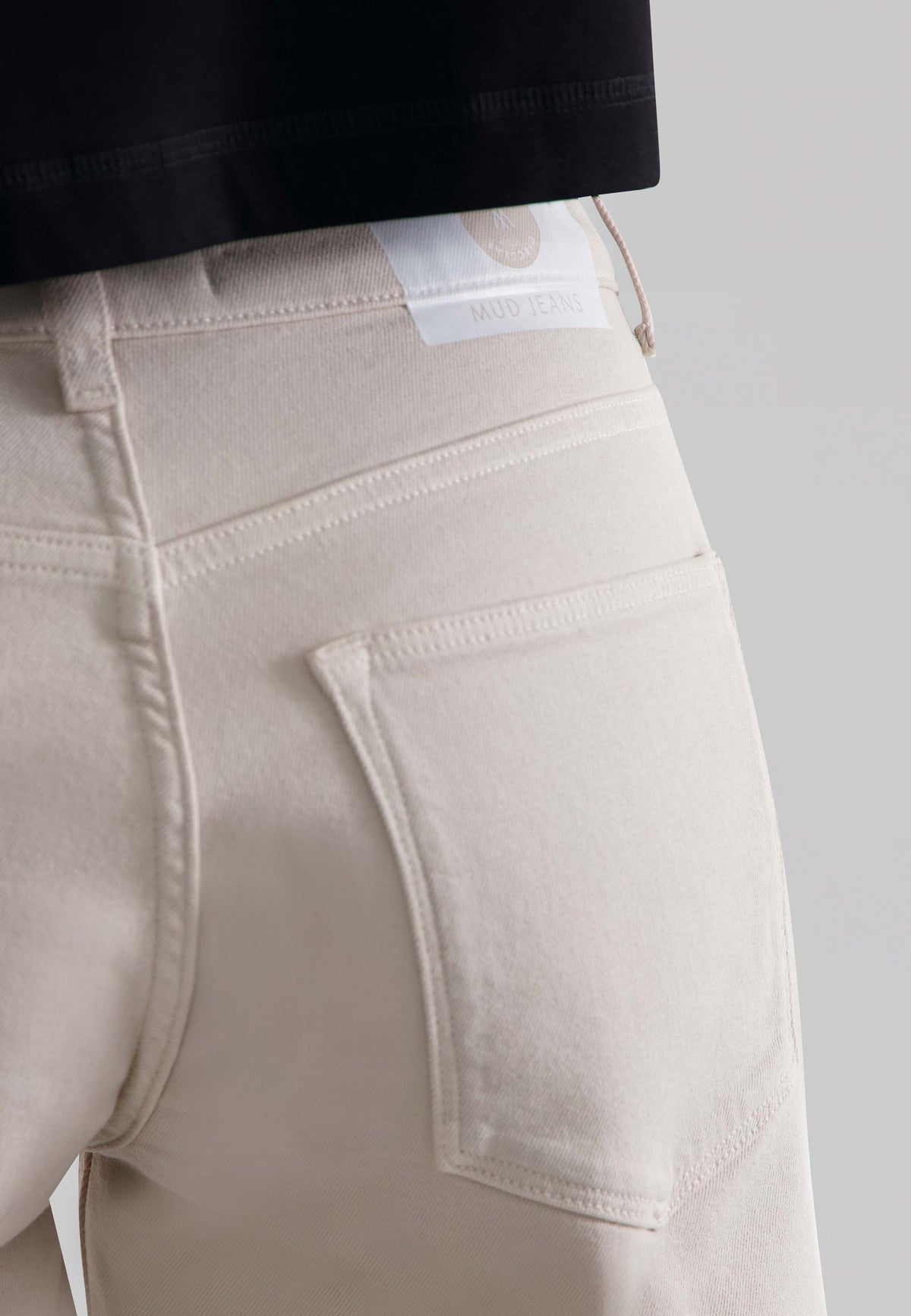 Beige MUD Jeans made from organic cotton featuring a classic pocket detail, shown worn with a black top.
