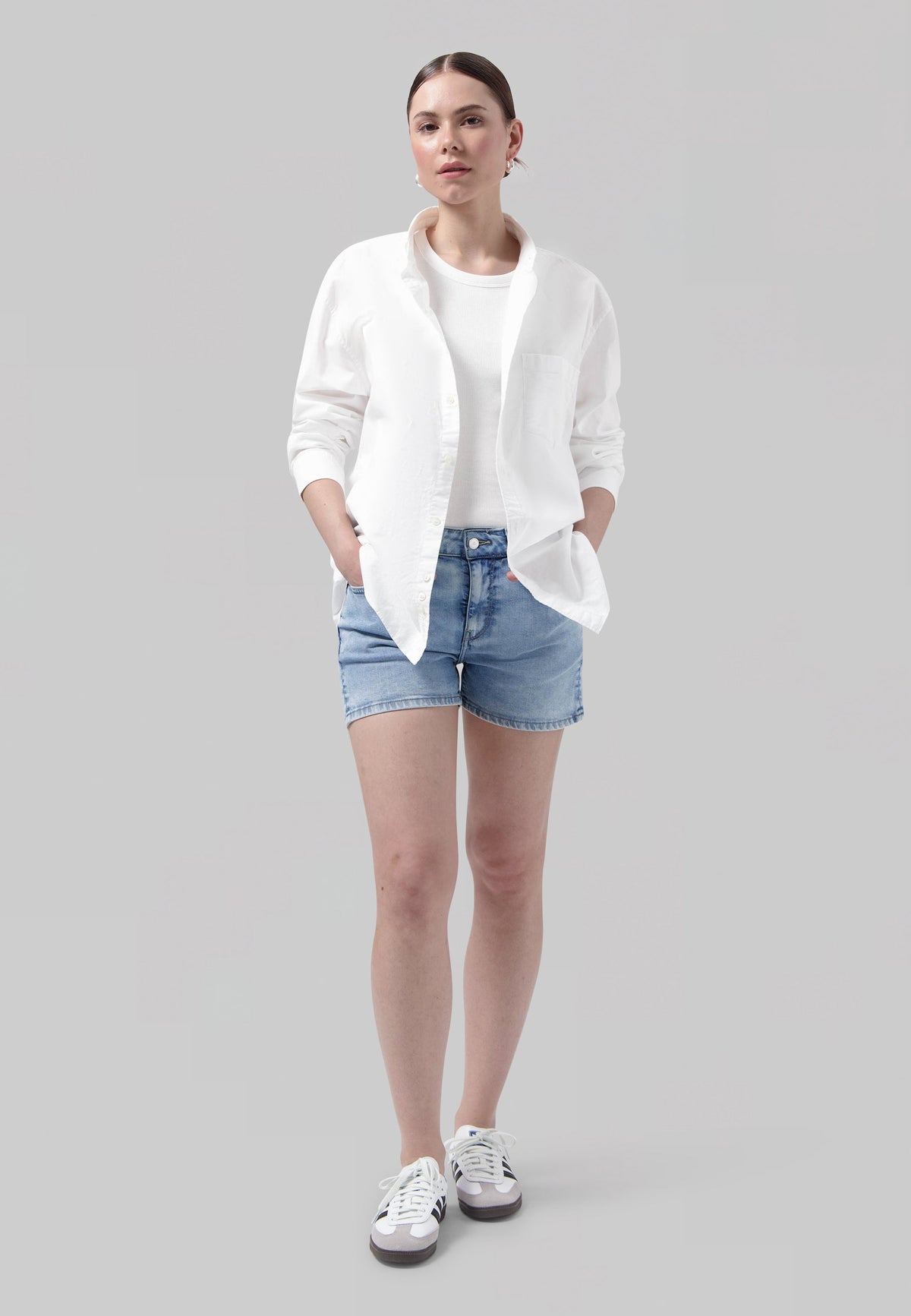 Casual summer outfit featuring light blue denim shorts, white shirt, and sneakers, perfect for a relaxed, stylish look.