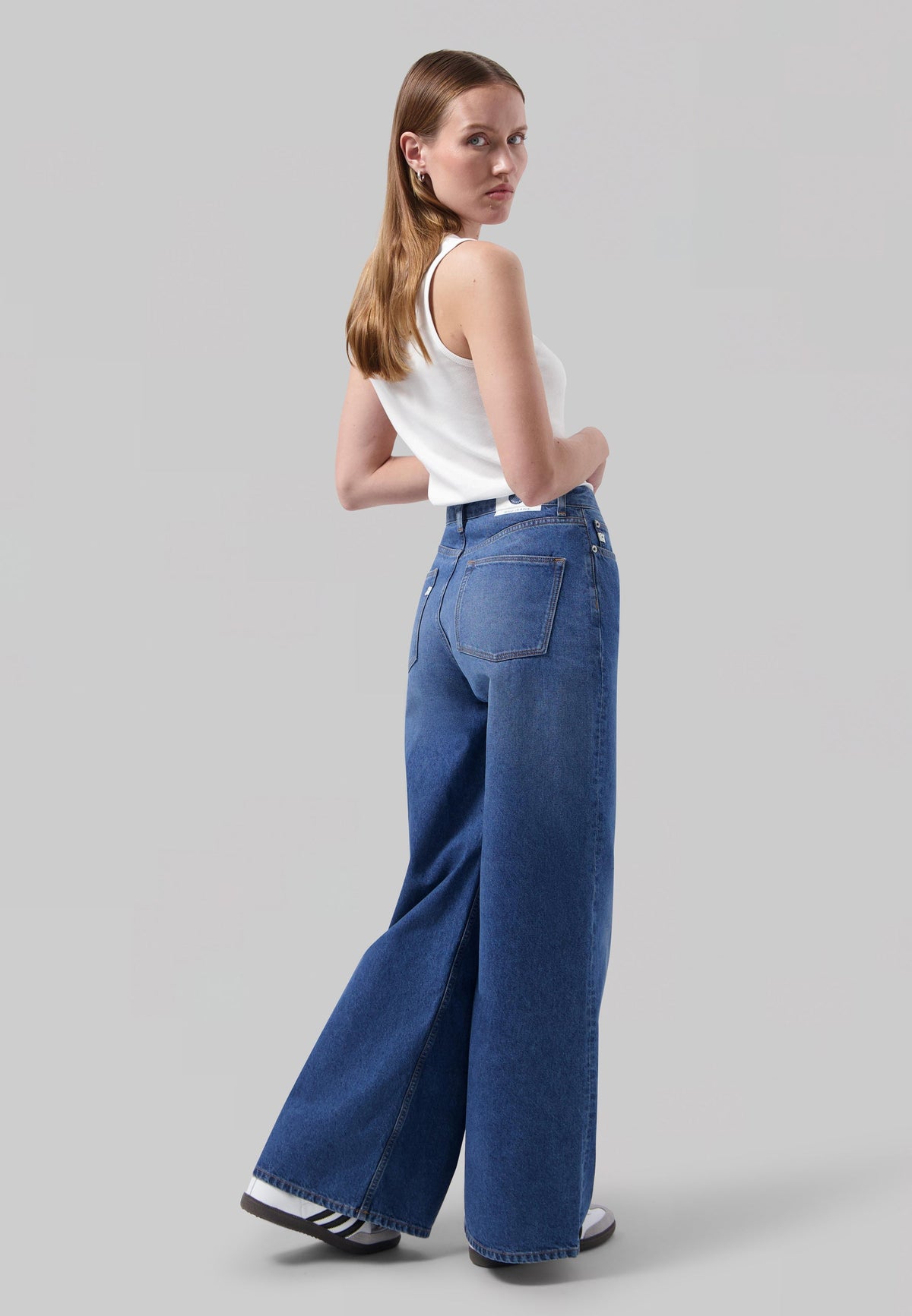 Wide-leg medium blue jeans paired with a white sleeveless top, showcasing a back view on a neutral background.