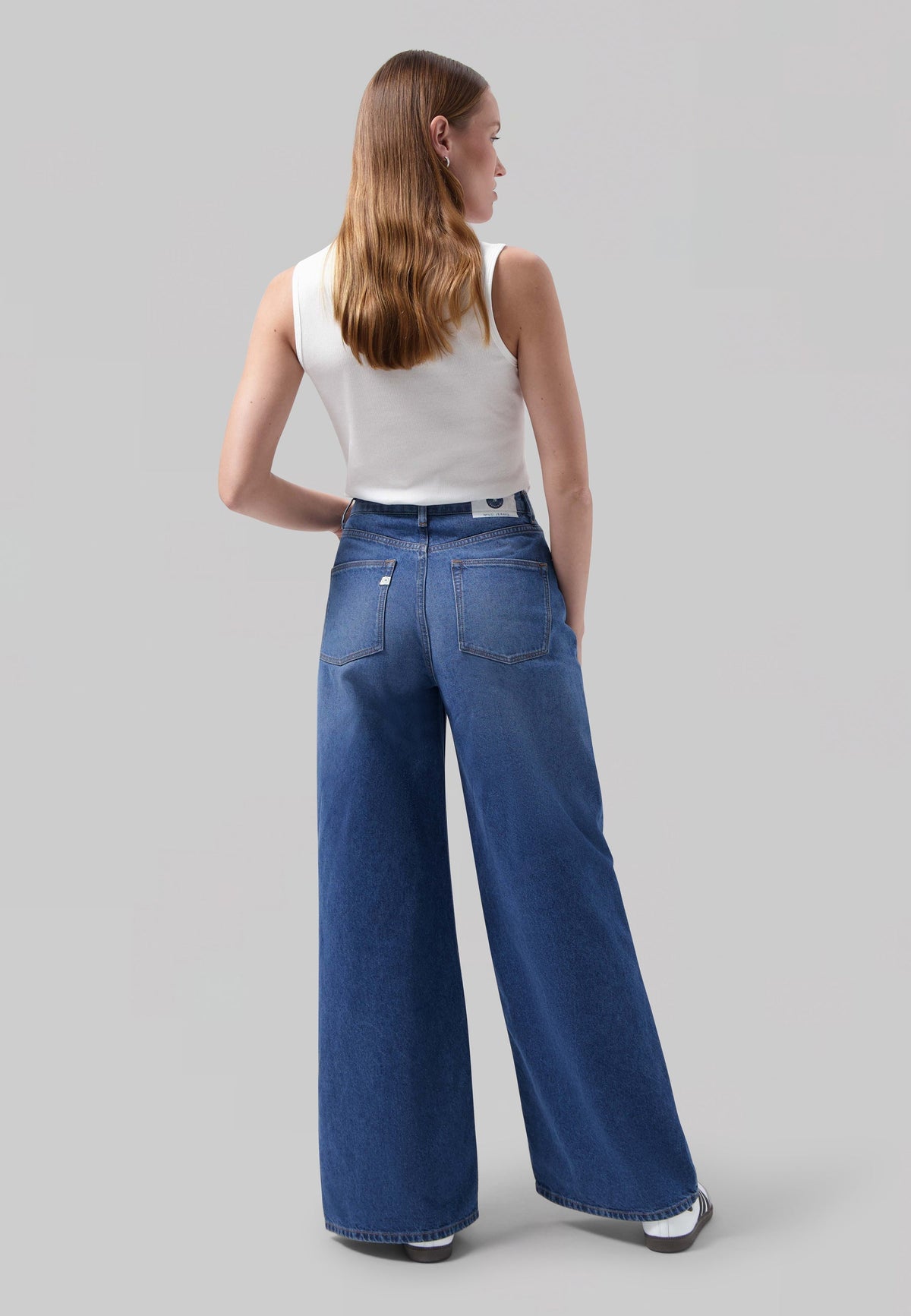 Wide-leg blue denim jeans paired with a sleeveless white top, showing a back view with long, brown hair.
