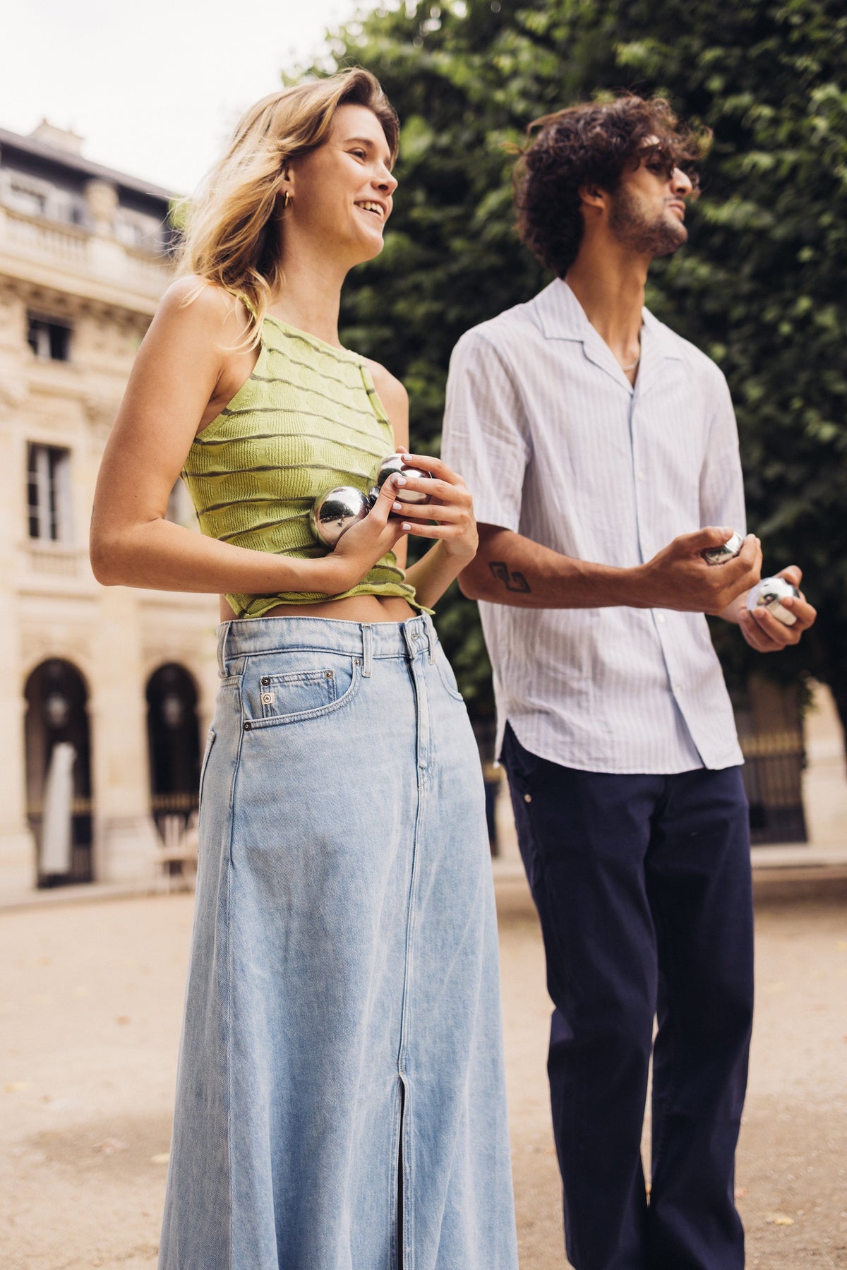 Casual summer fashion with woman in green textured top and light denim skirt beside man in striped white shirt.