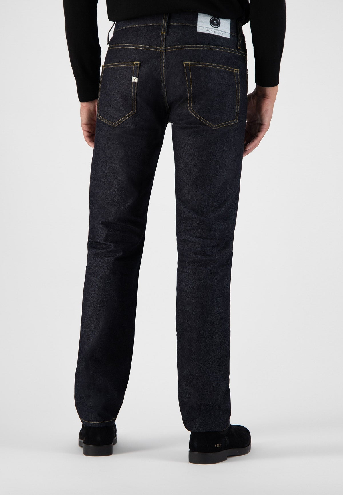 Sustainable MUD Jeans in dark blue denim, crafted ethically, paired with a black high-neck sweater, rear view.