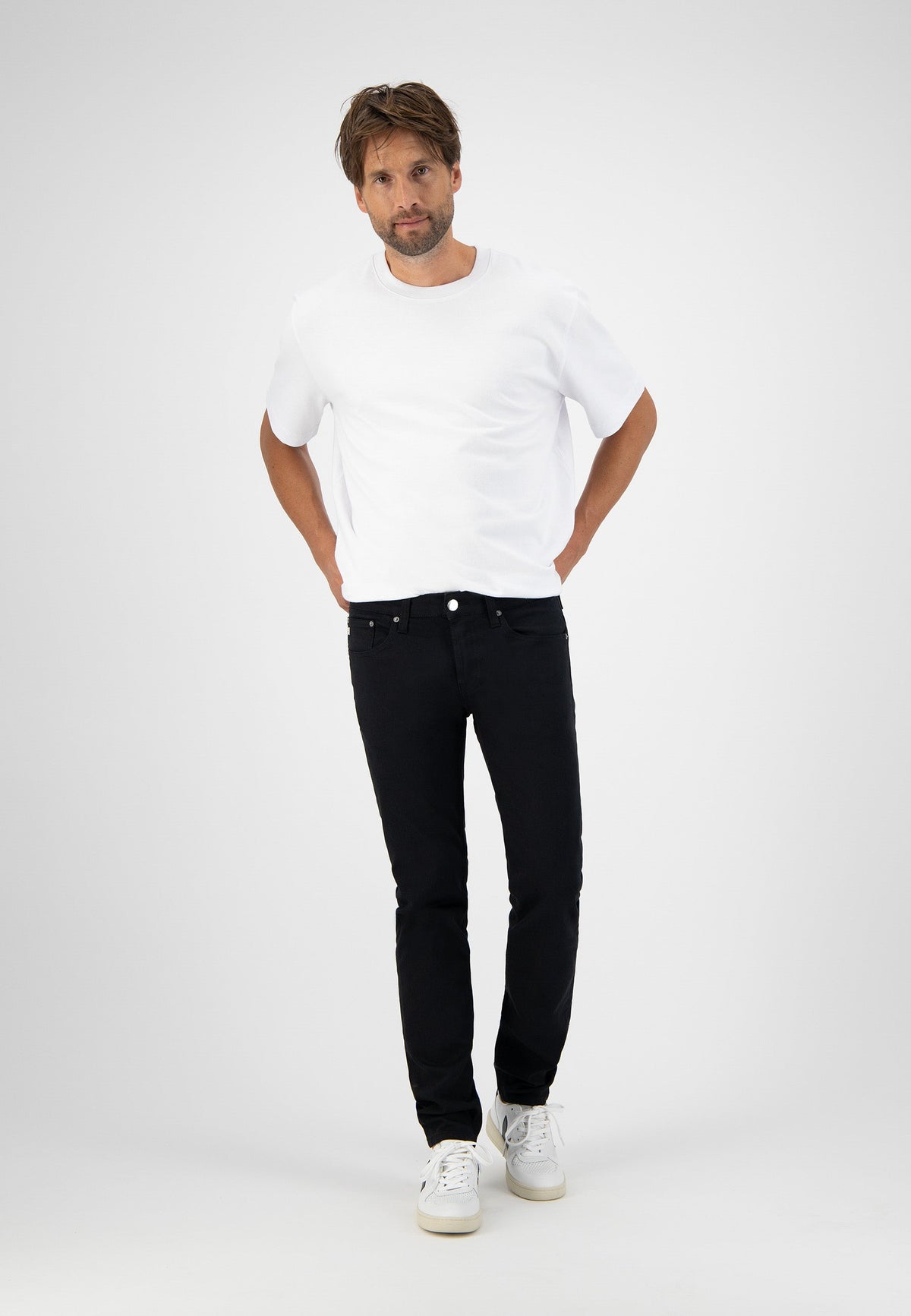 Sustainable MUD Jeans in black denim, crafted ethically, paired with a white T-shirt and sneakers for a casual look.
