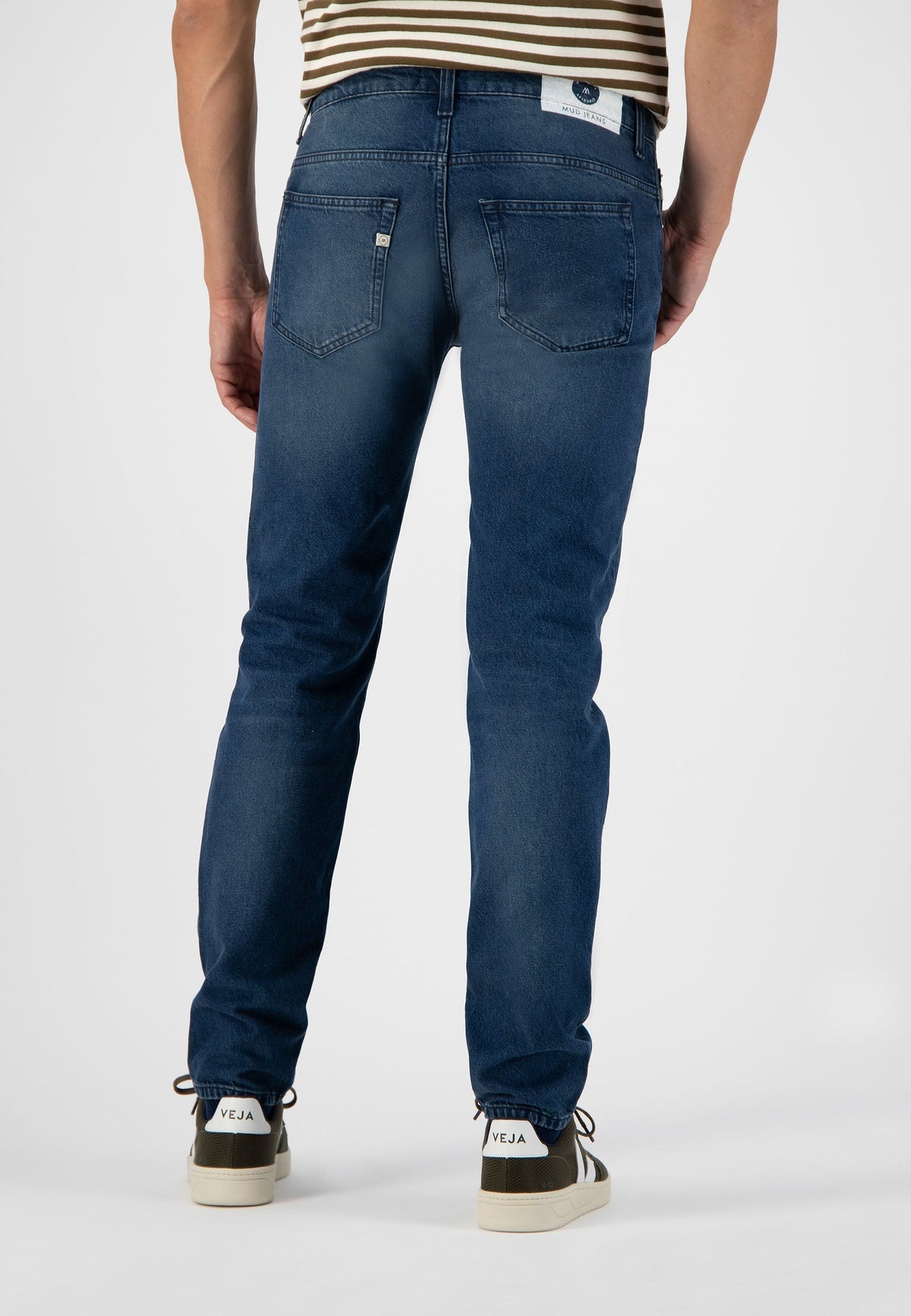 Sustainable MUD Jeans in deep blue, crafted ethically from organic cotton, featuring a relaxed fit worn with beige sandals.