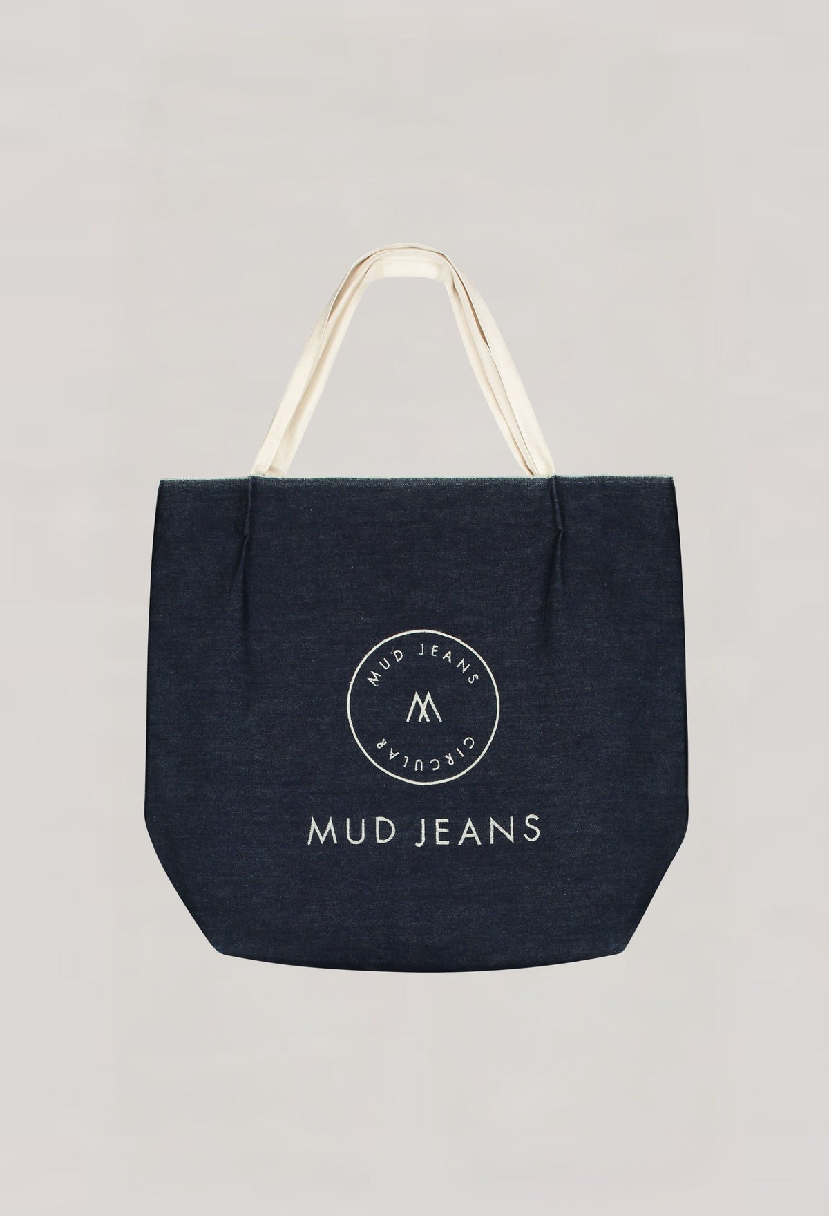 Dark blue denim tote bag from MUD Jeans, featuring cream handles and circular logo, emphasizing sustainable fashion.