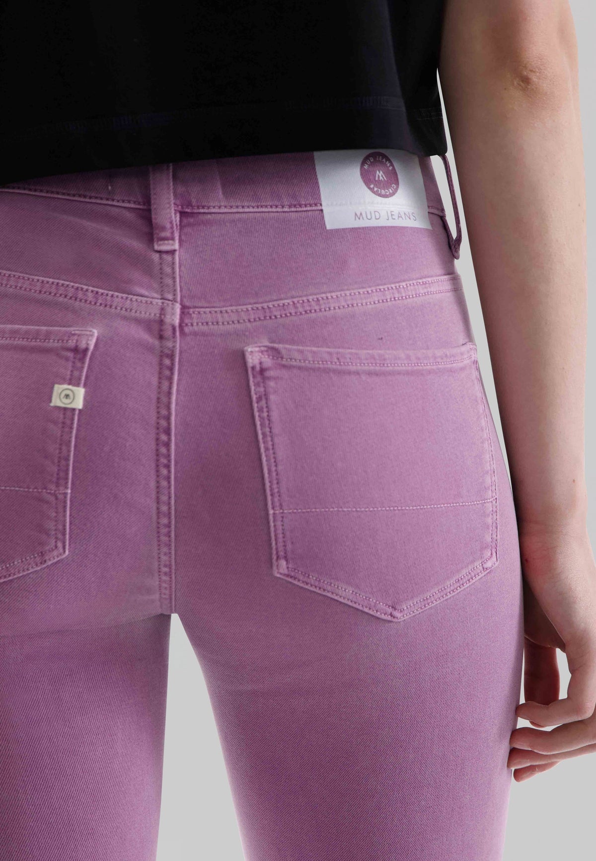 Person wearing pastel pink eco-friendly denim jeans with a black top, showing detailed stitching and pocket design.