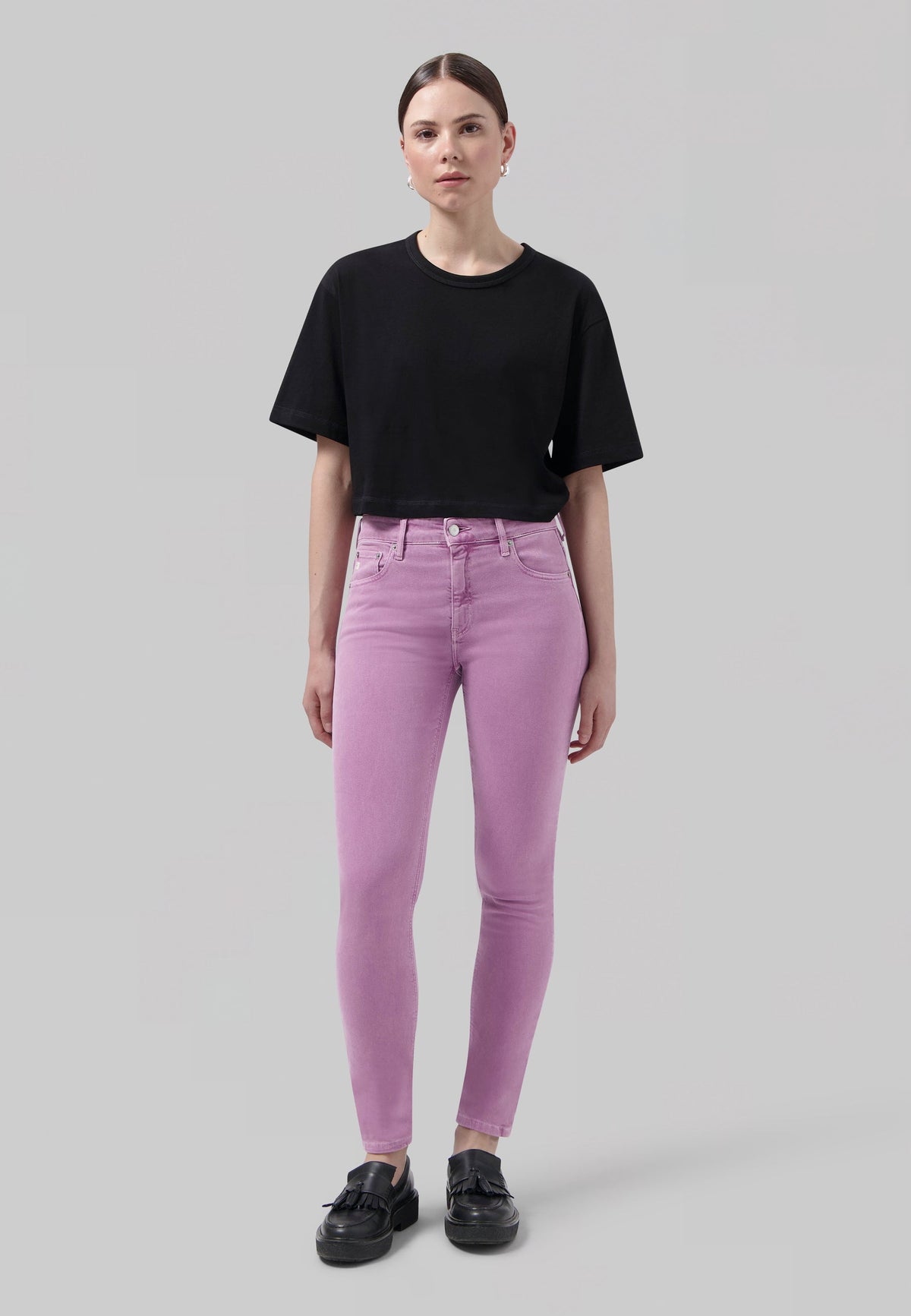 Casual outfit with a black cropped T-shirt paired with lavender skinny jeans and black loafers, showcasing modern fashion.