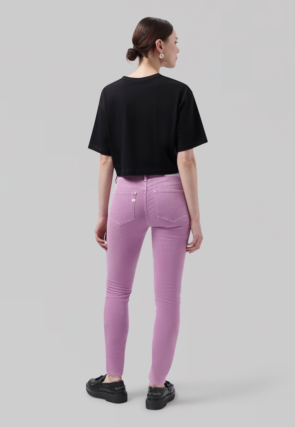 Woman wearing a black cropped top paired with pastel purple skinny jeans and black platform shoes, highlighting casual style.