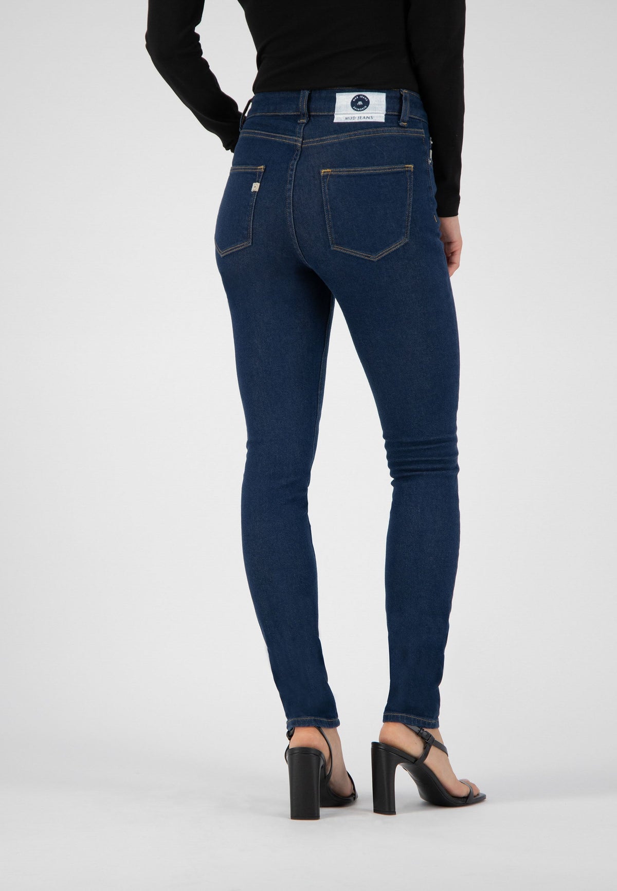 Slim-fit MUD Jeans made from organic cotton, showcasing back view of dark blue denim styled with a black long-sleeve top.