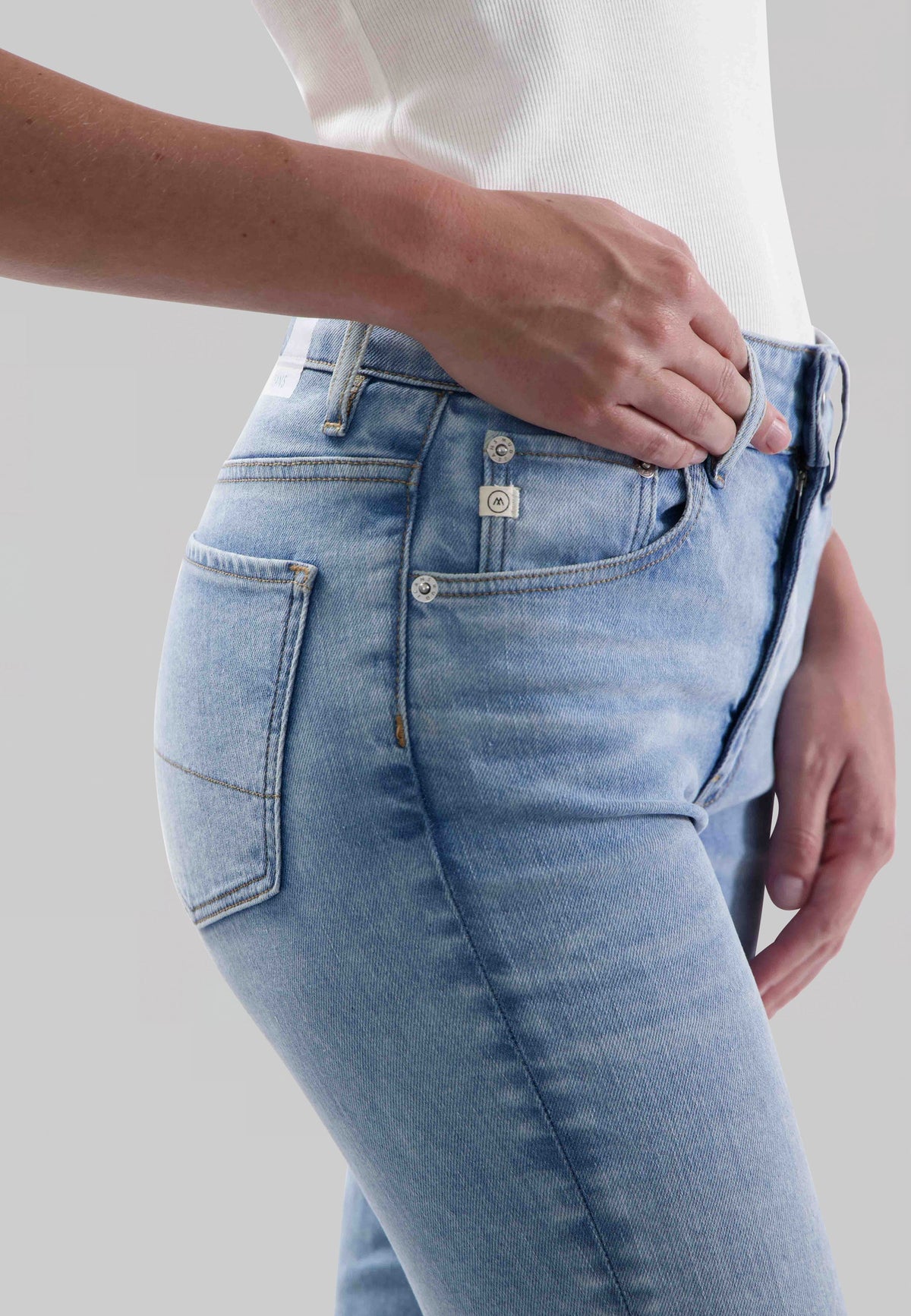 Close-up of light blue, slim-fit denim jeans worn with a white ribbed tank top, highlighting the pocket and button details.