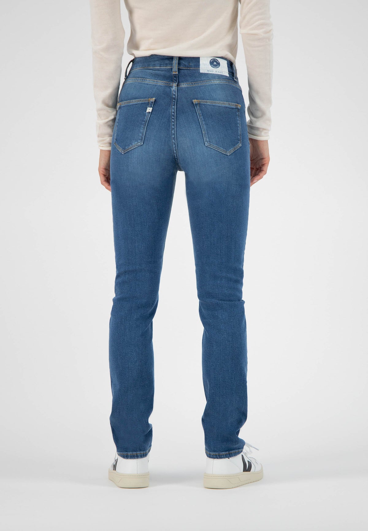 Person wearing sustainable blue skinny jeans from MUD Jeans, styled with a cream long-sleeve top, shown from the back.