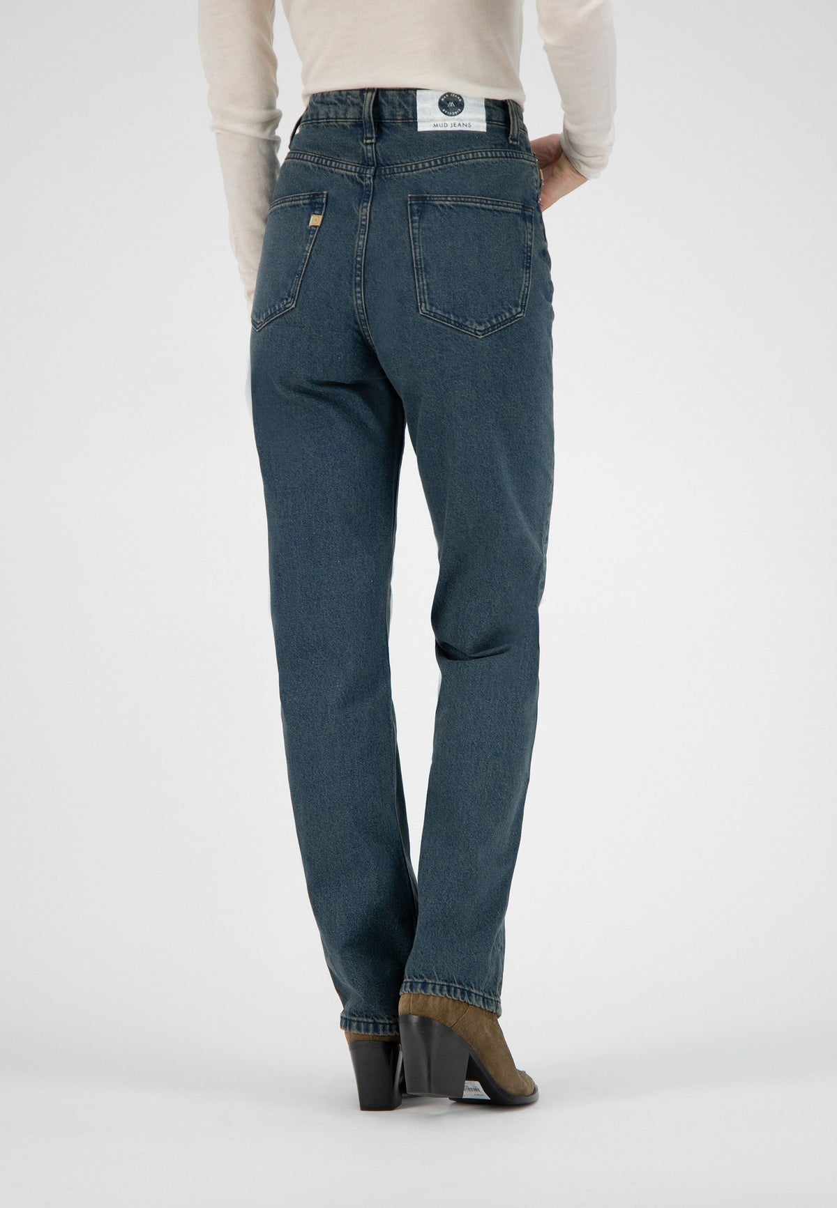 Back view of sustainable MUD Jeans made from organic cotton in a classic blue wash, paired with brown suede heeled boots.