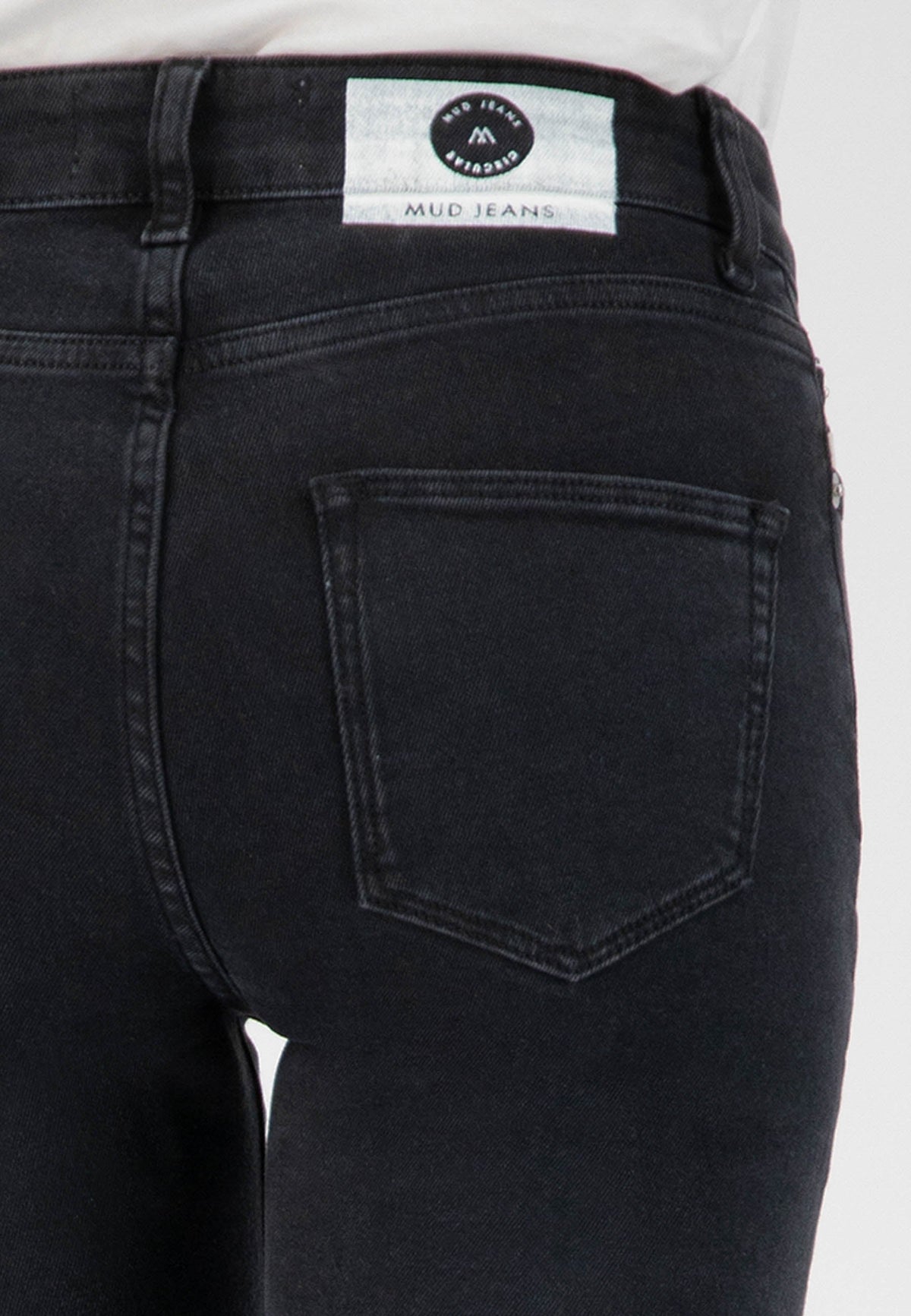 Close-up of sustainable, dark indigo MUD Jeans showing the back pocket detail and fabric label with organic materials.
