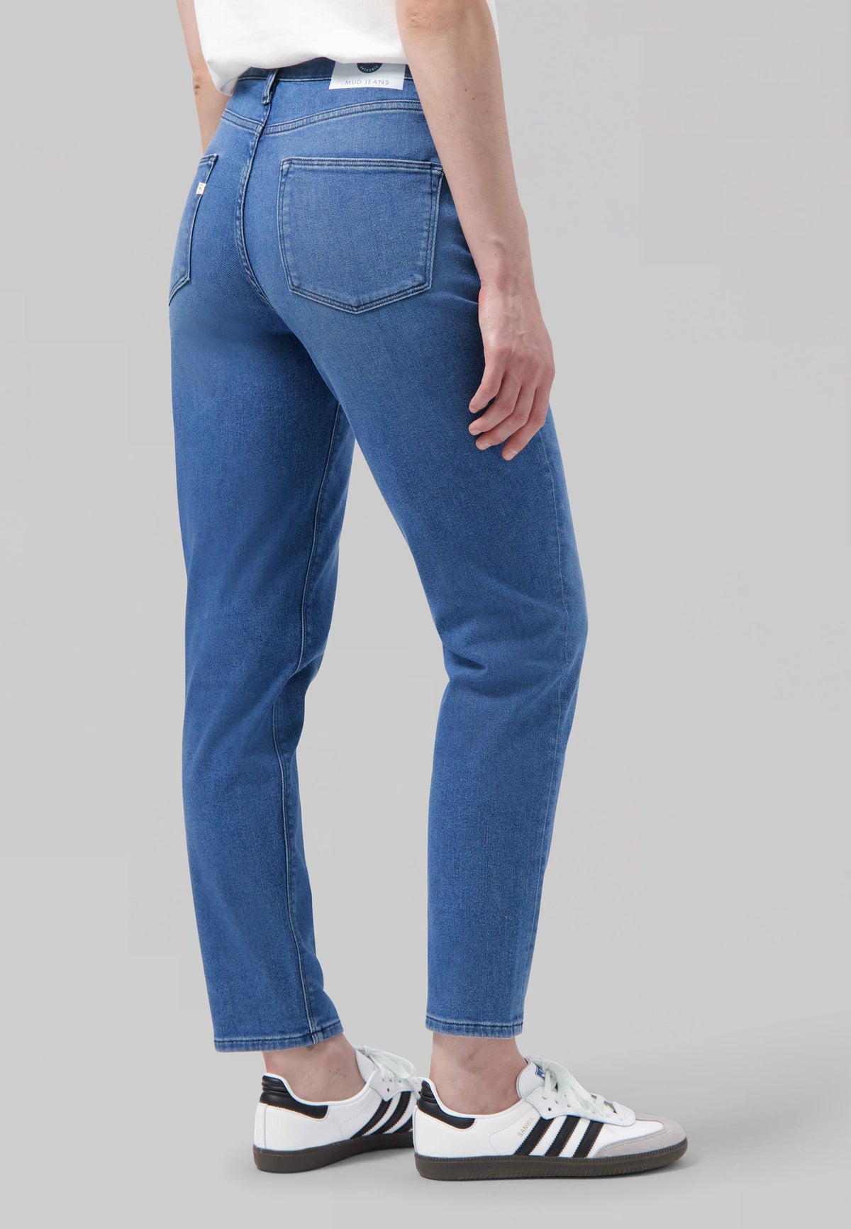 Person wearing eco-friendly MUD Jeans made from organic cotton, showcasing medium blue denim with white casual sneakers.