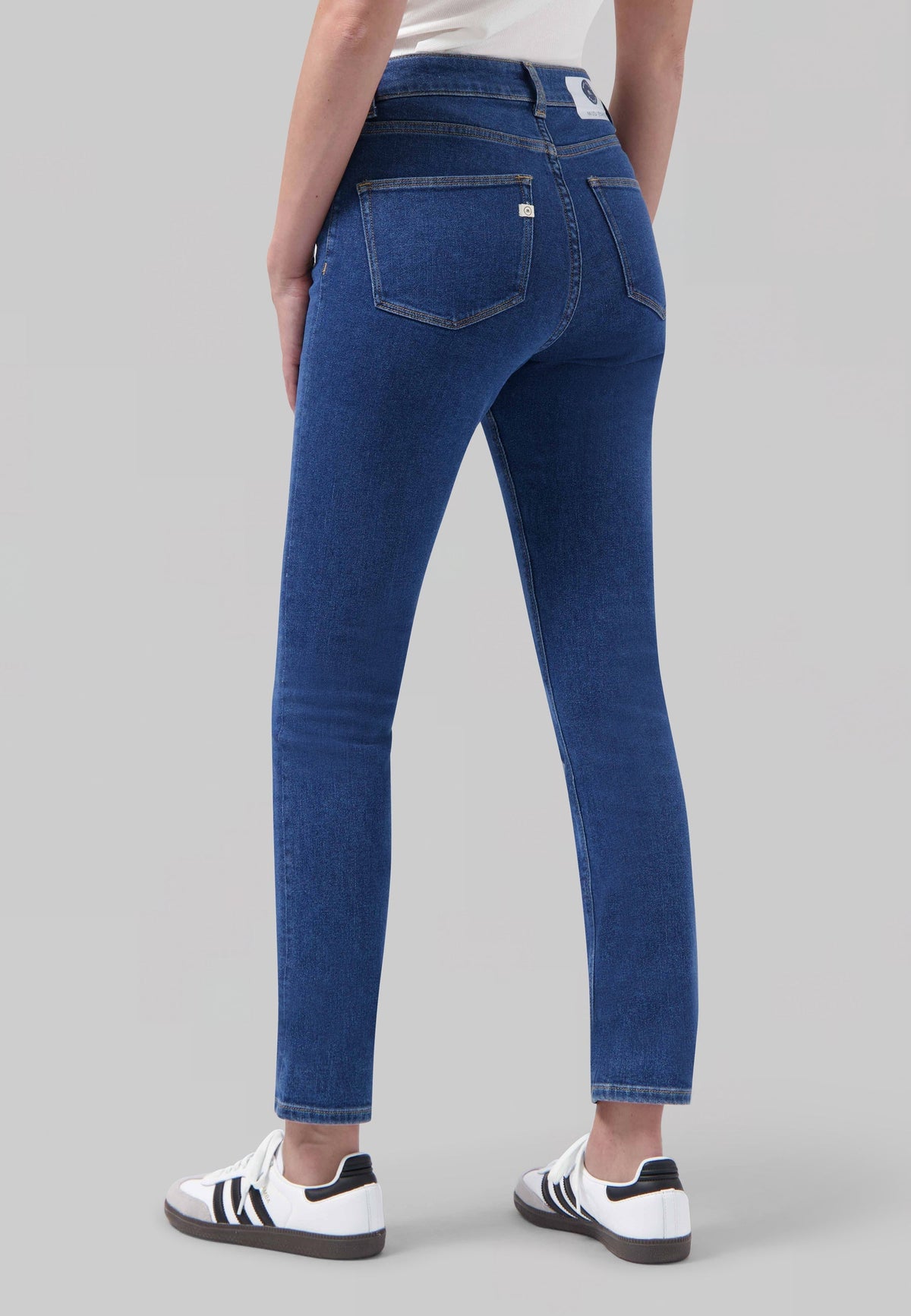 Slim-fit blue jeans made from sustainable denim, shown from the back with a white casual sneaker and a plain white top.