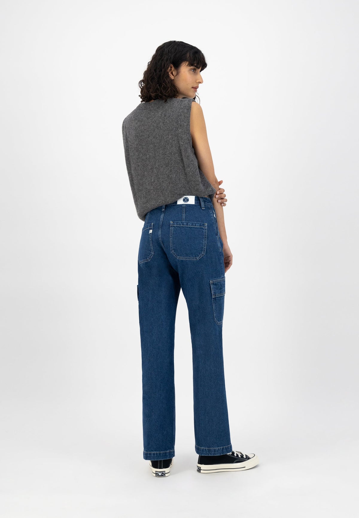 A woman wearing a sleeveless gray woolen top and blue denim jeans with a relaxed fit, styled with black sneakers.