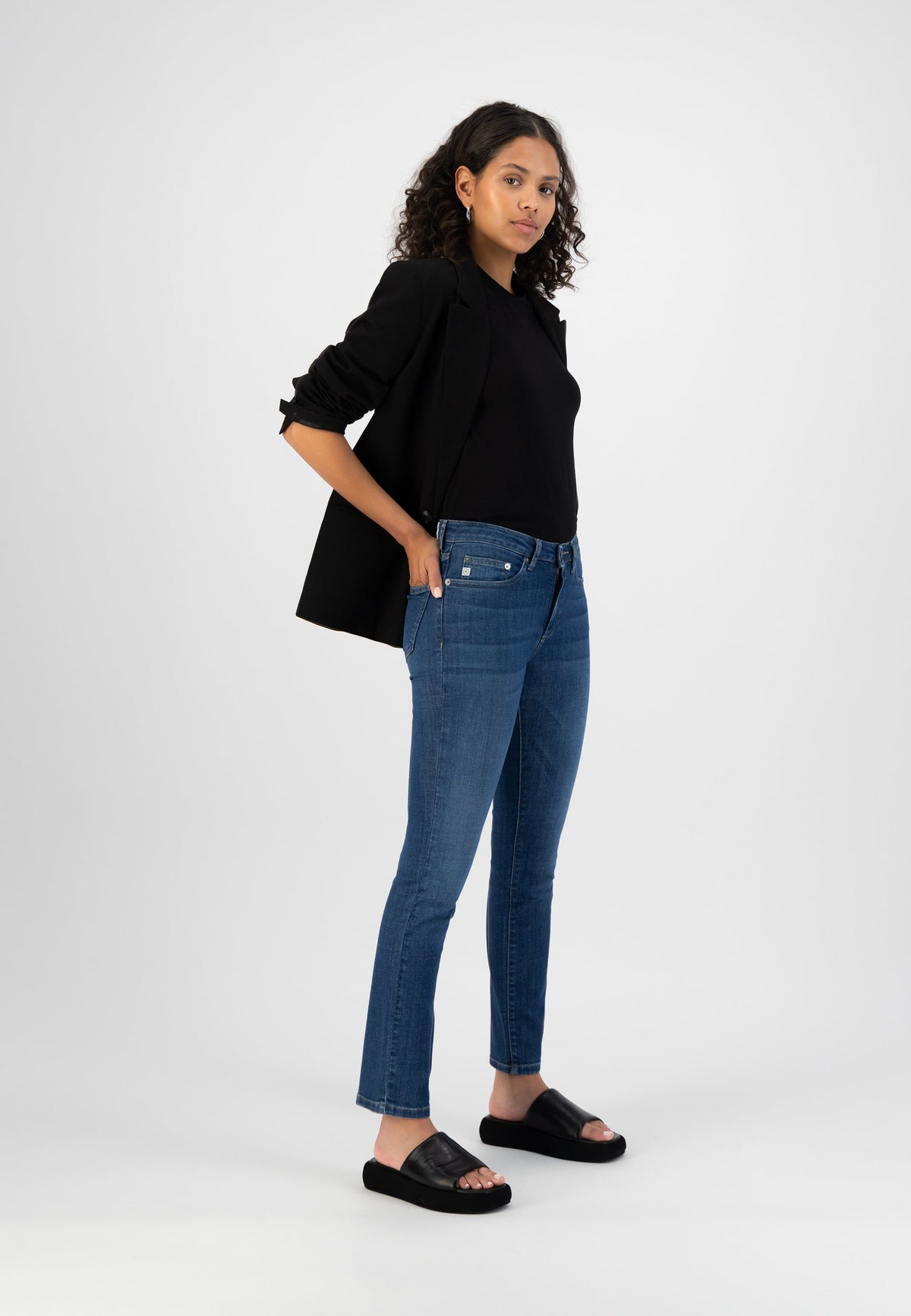Modern casual outfit with dark blazer, black top, slim-fit blue jeans, and black slide sandals, showcasing contemporary style.