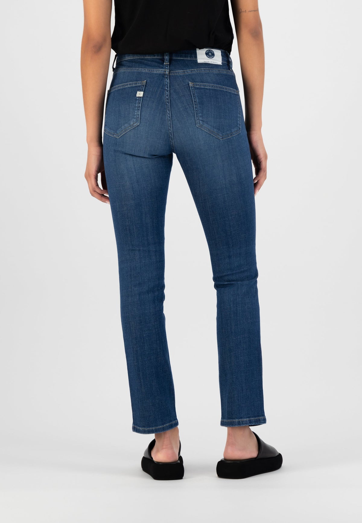 Model wearing eco-friendly dark blue straight-leg denim jeans, back view, paired with a black sleeveless top.
