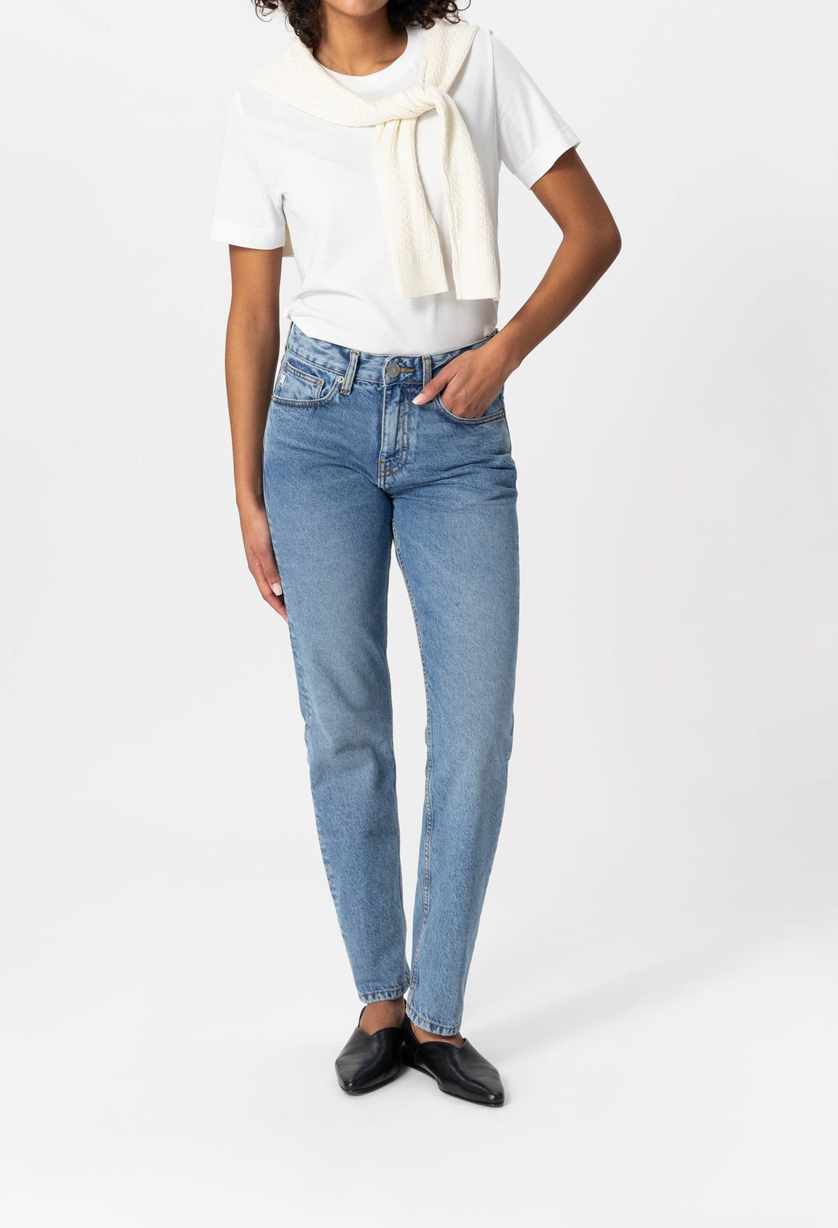Casual outfit with light blue high-waisted jeans, white T-shirt, and black flats, featuring an elegantly draped cream sweater.