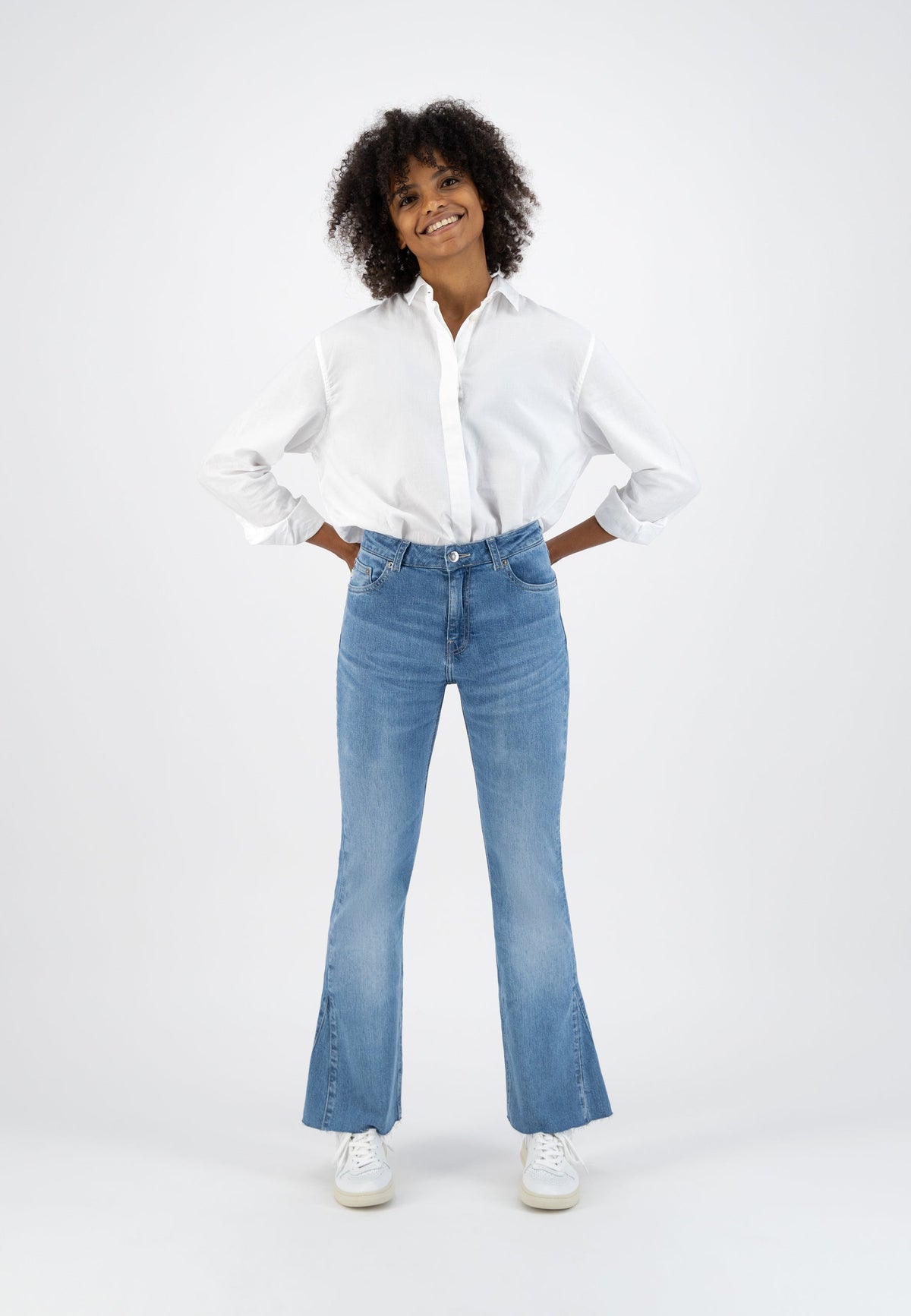 Casual outfit featuring light blue flared jeans paired with a crisp white button-up shirt and white sneakers.