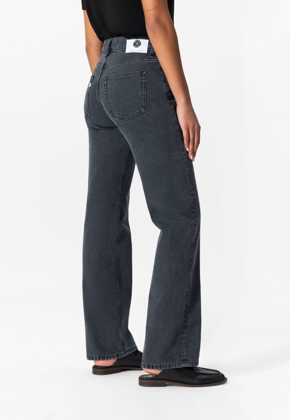 Dark gray organic cotton MUD Jeans with a straight leg cut, worn by a person in a black short-sleeve top and sandals.