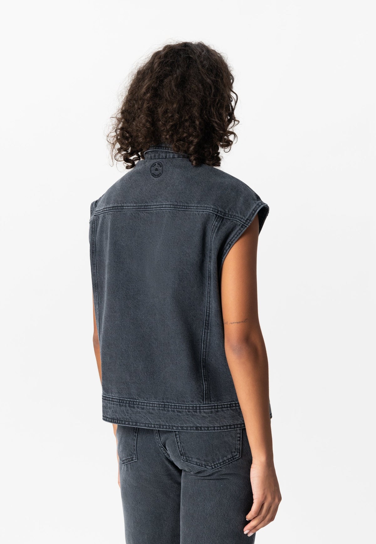 Back view of a person wearing a sleeveless black denim vest paired with matching black jeans, showcasing casual fashion style.