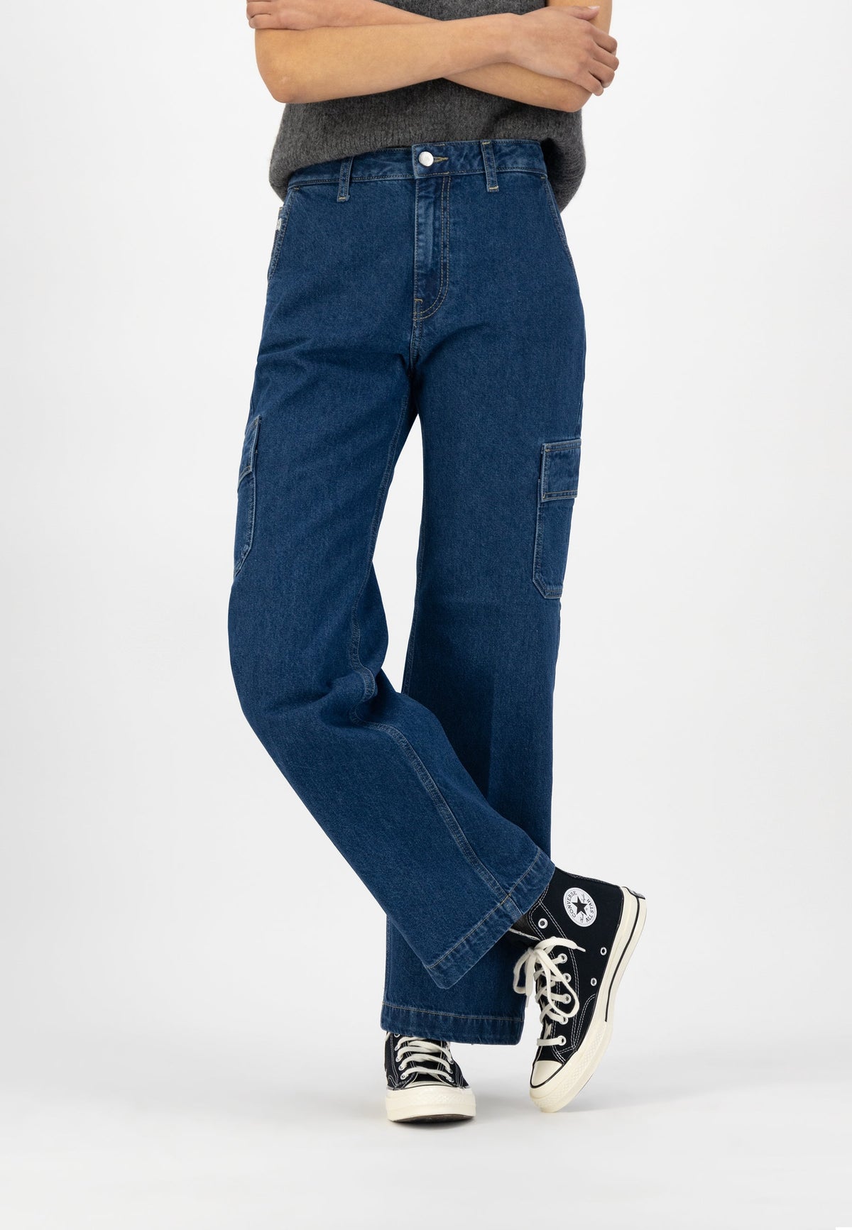 Wide-leg blue denim jeans with cargo pockets, paired with black-and-white high-top sneakers and a gray sweater.