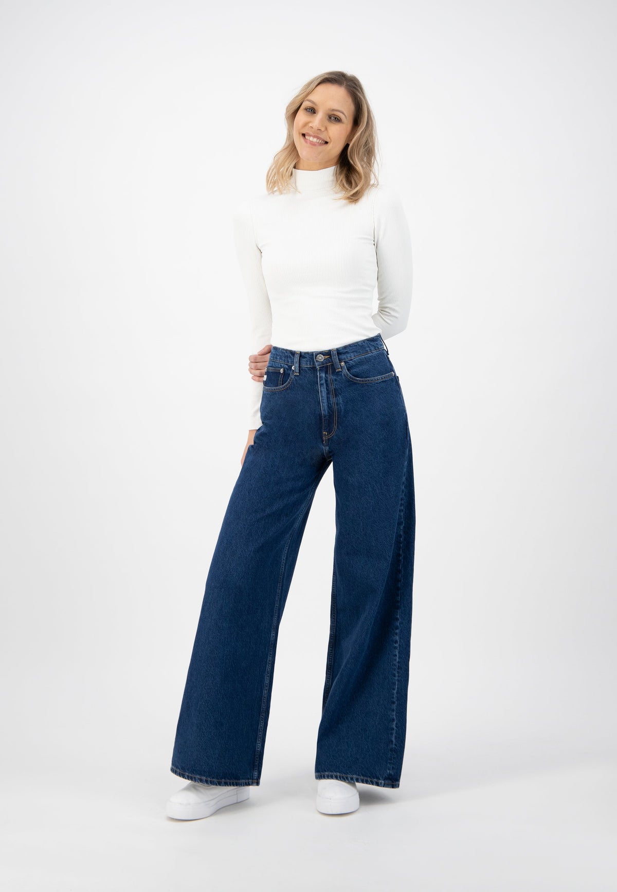 Wide-leg blue jeans worn with a fitted long-sleeve white turtleneck top, styled with casual white sneakers.
