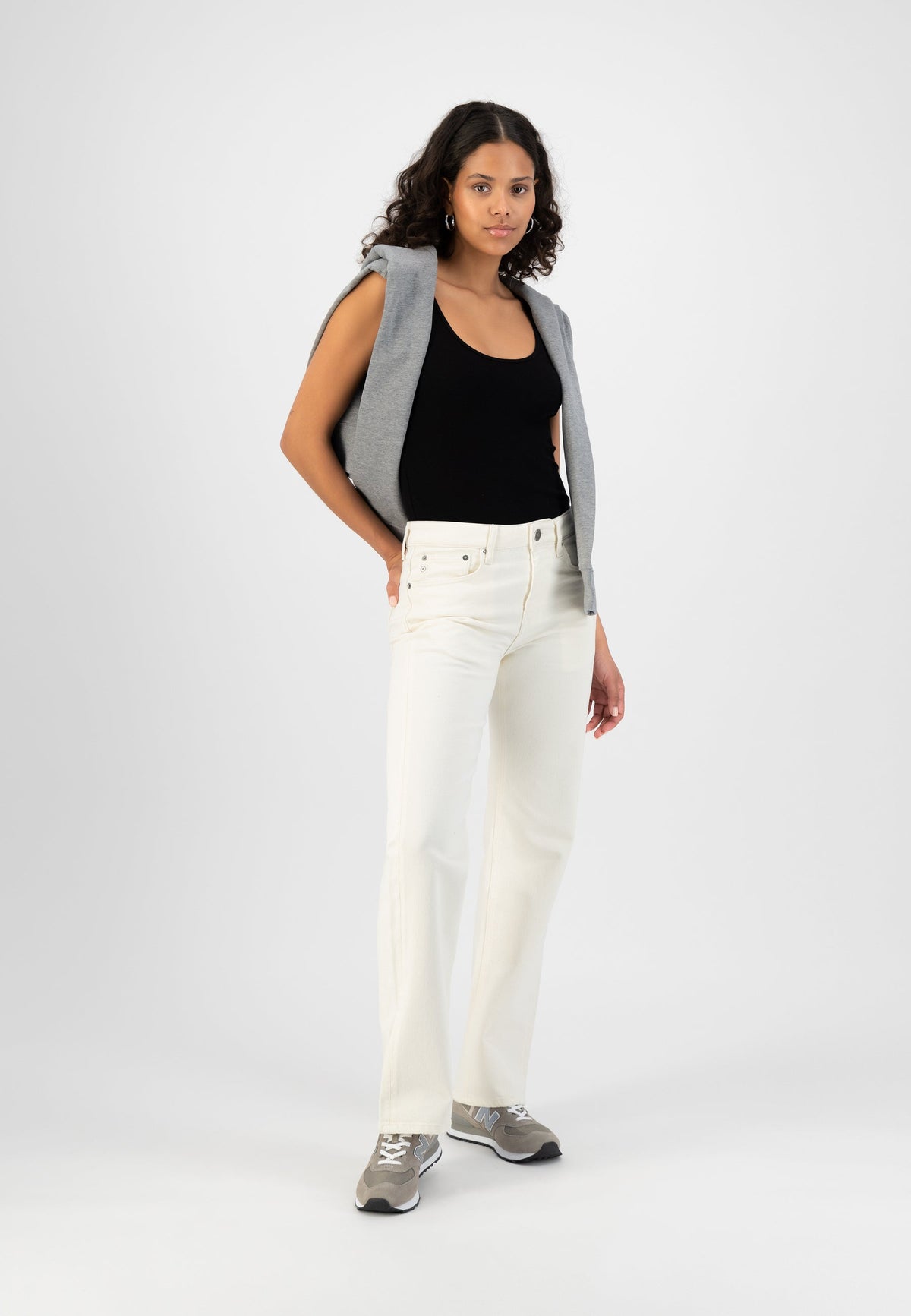 Casual outfit with white high-waisted jeans, black tank top, gray sweater over shoulders, and gray sneakers.