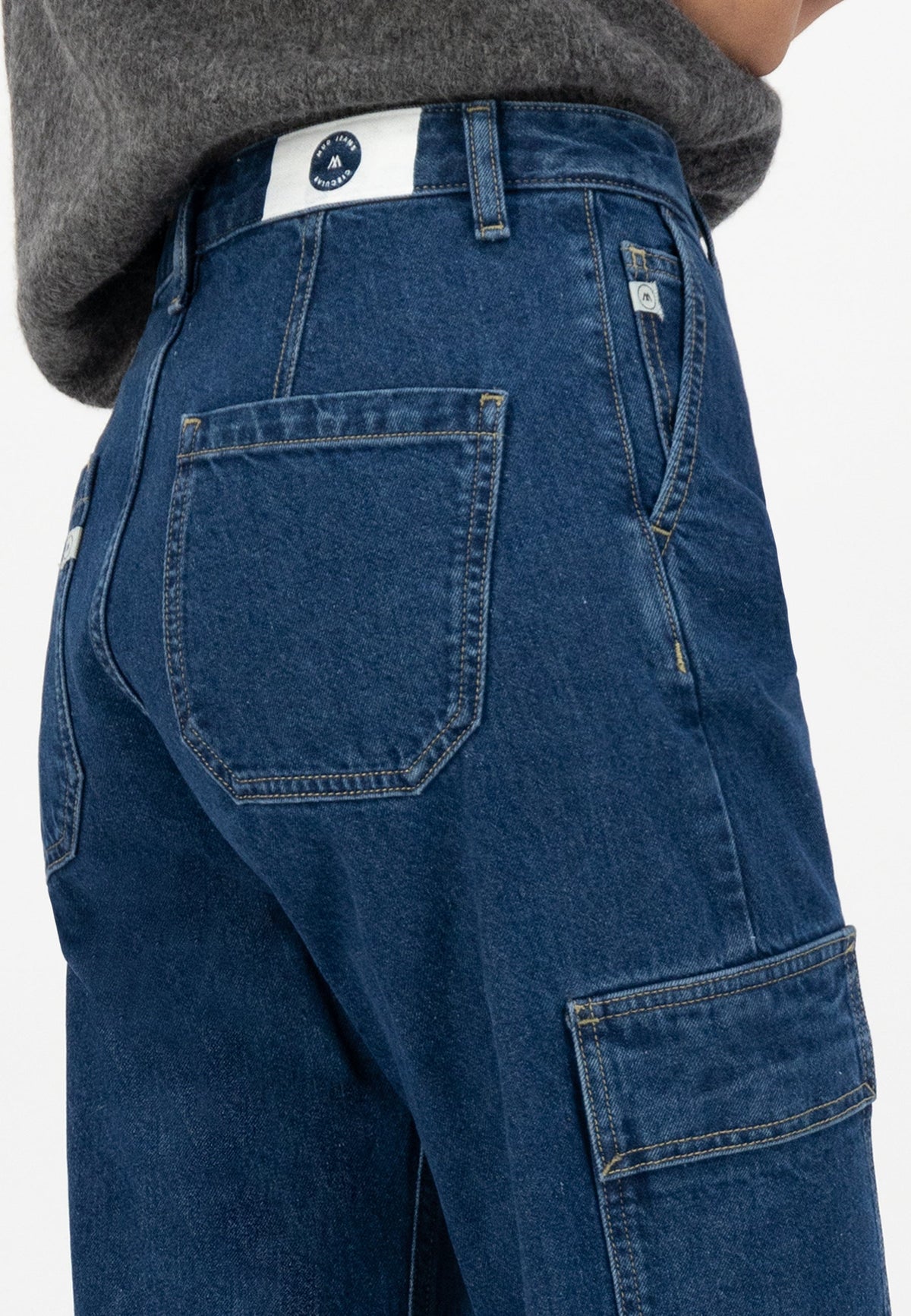 Close-up of blue denim cargo jeans with detailed stitching and a back pocket, paired with a gray wool sweater.