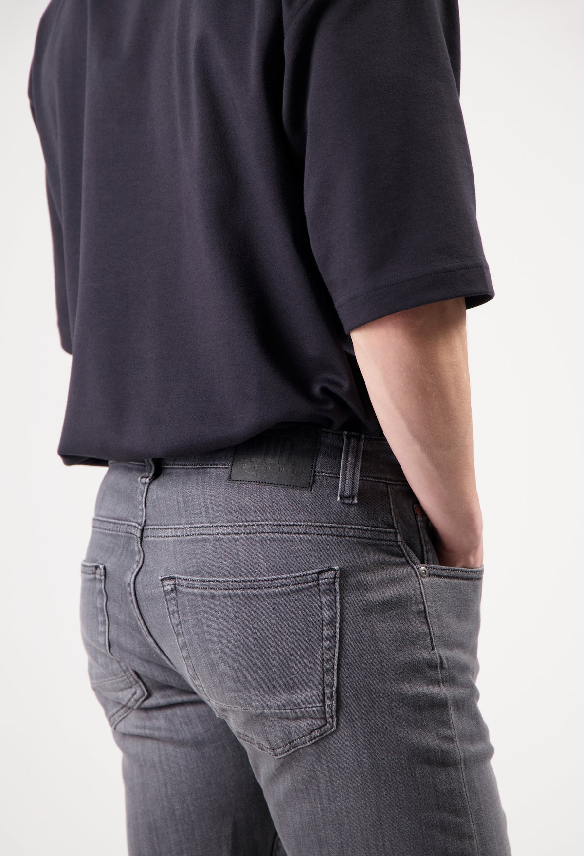 Sustainable MUD Jeans in dark blue denim, crafted ethically, paired with a casual gray T-shirt and white sneakers.