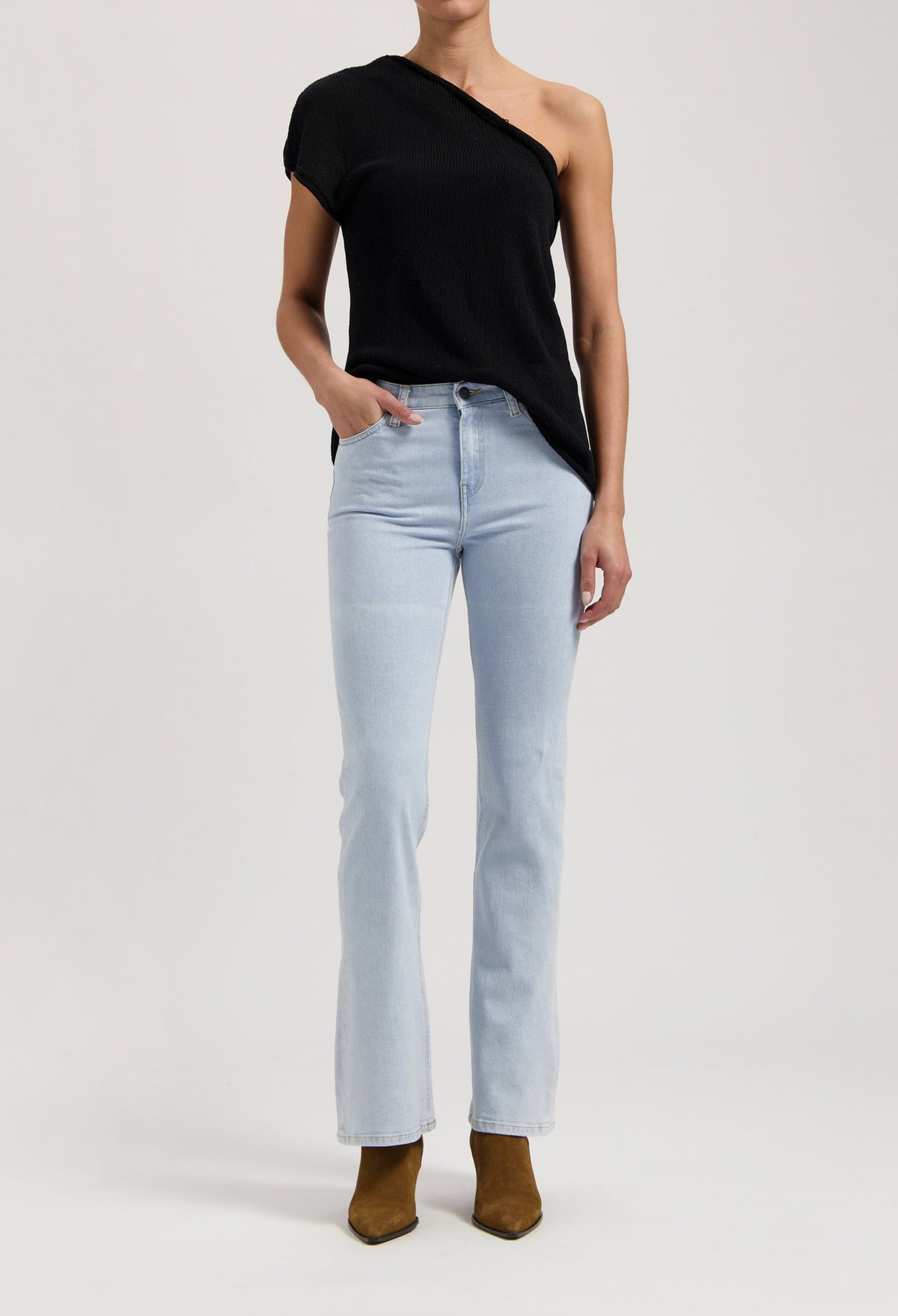 Stylish black one-shoulder top paired with light wash, high-waisted jeans and brown suede ankle boots.