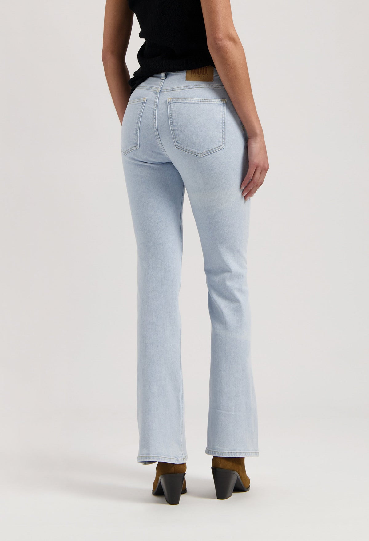 Woman wearing light blue straight-leg jeans paired with a black sleeveless top and brown heeled boots, shown from behind.