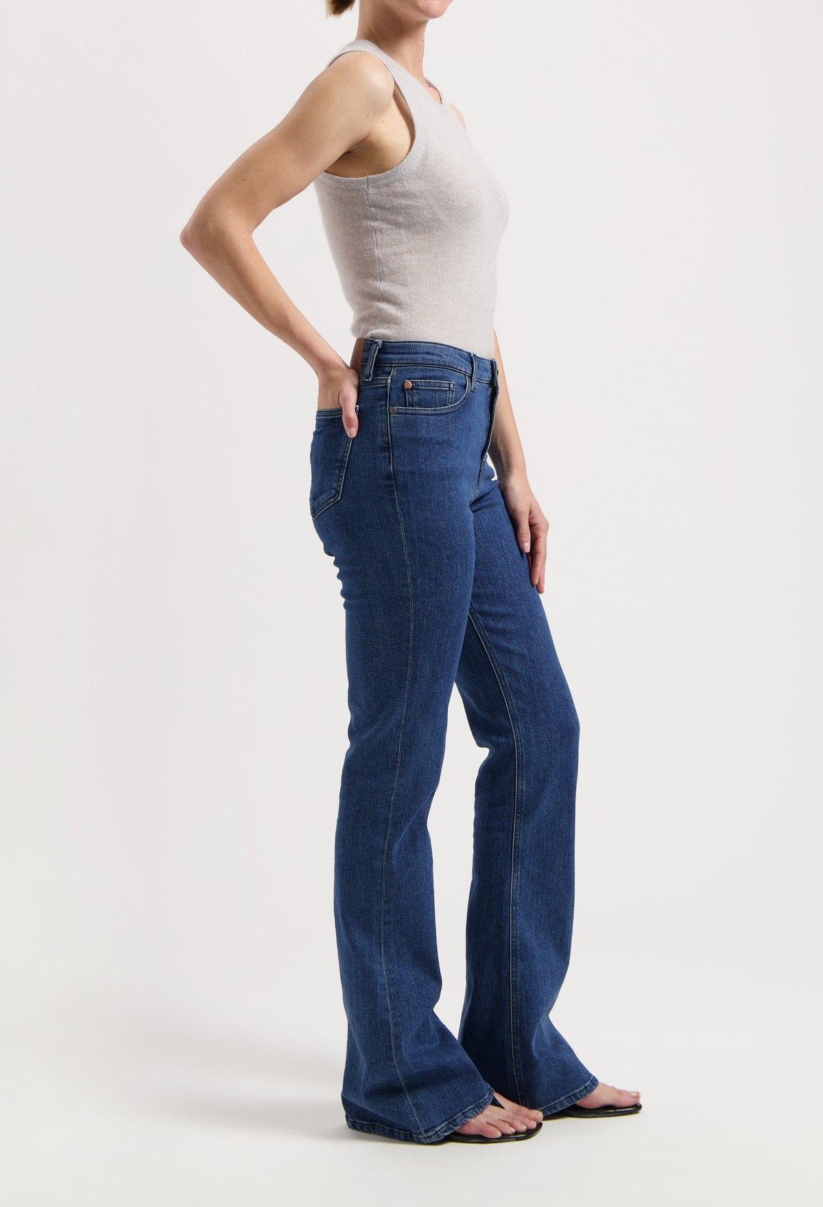 Model wearing a sleeveless beige top with blue high-waisted bootcut jeans, showcasing casual style and fit.