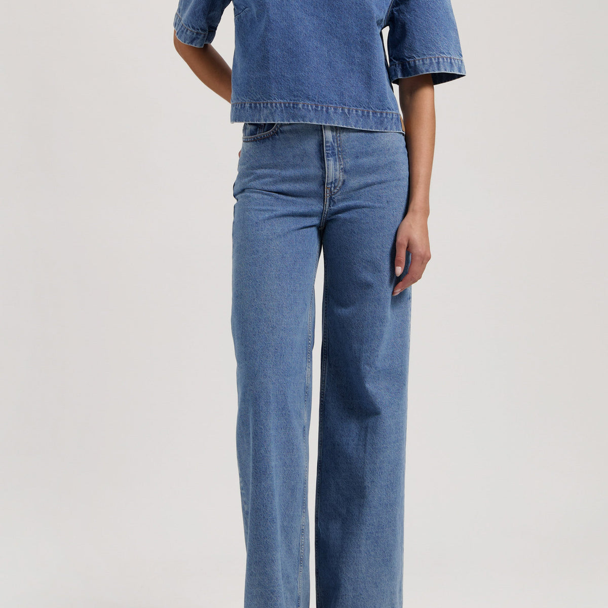 Model wearing blue denim two-piece outfit with short-sleeve top and wide-leg jeans, showcasing casual fashion style.