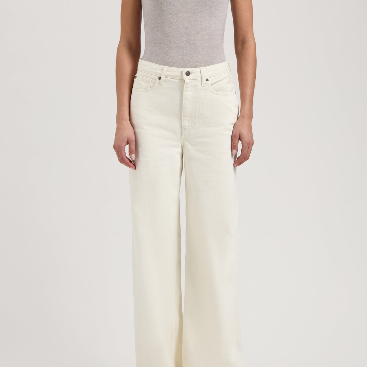 Woman wearing light gray sleeveless top paired with high-waisted, wide-leg white denim jeans, showcasing modern casual fashion.