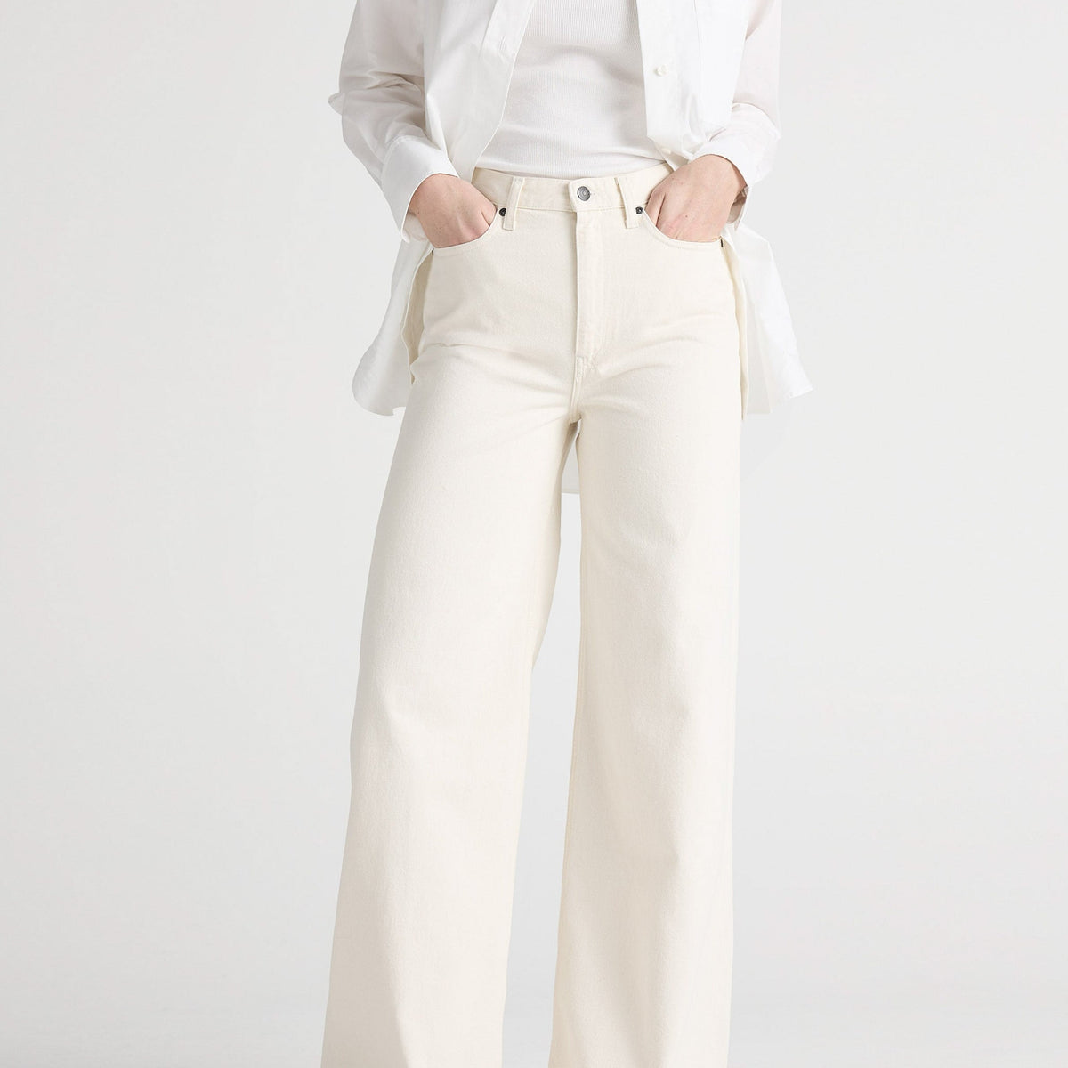 White wide-leg denim jeans paired with a tucked-in white tank top and unbuttoned shirt, worn with black sandals.