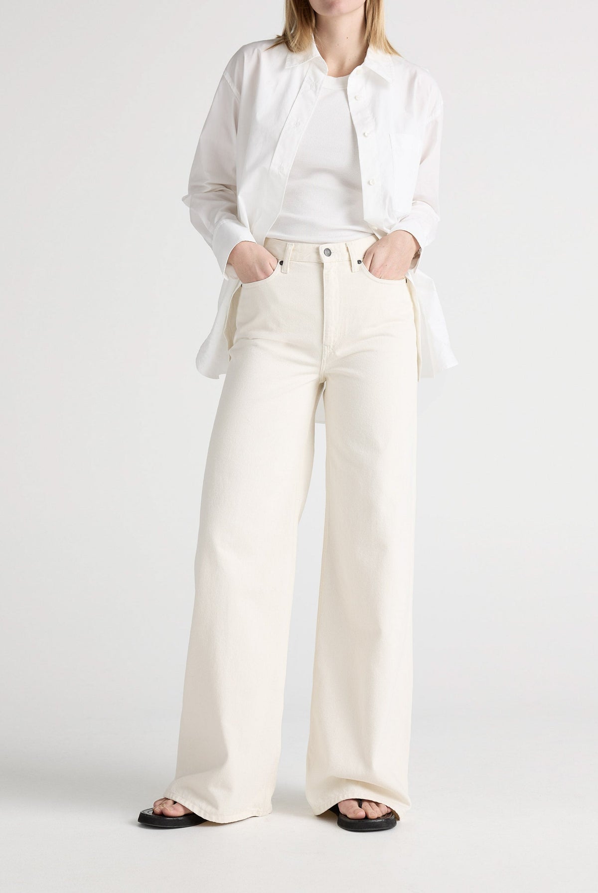 White wide-leg denim jeans paired with a tucked-in white tank top and unbuttoned shirt, worn with black sandals.