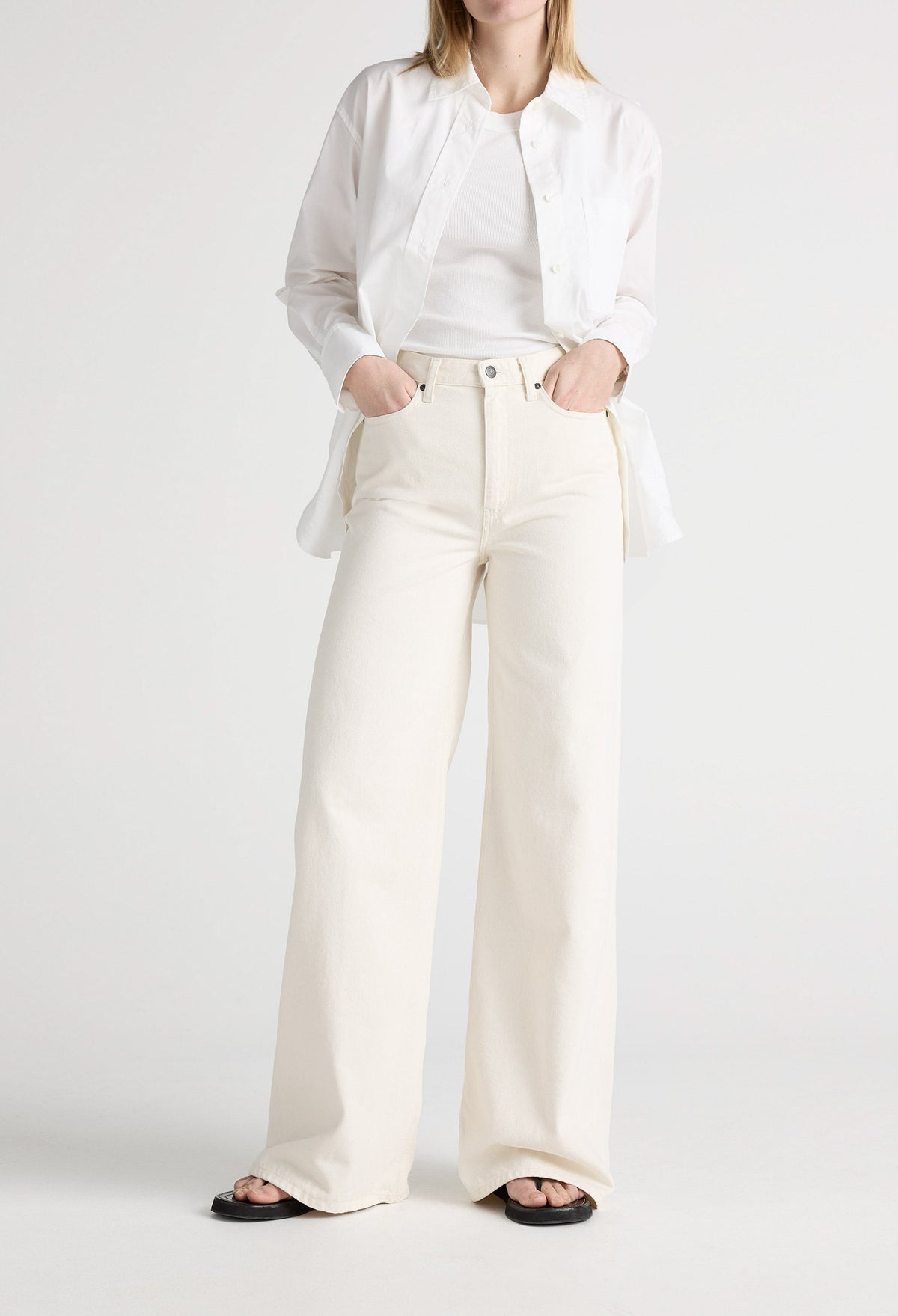 White wide-leg denim jeans paired with a tucked-in white tank top and unbuttoned shirt, worn with black sandals.
